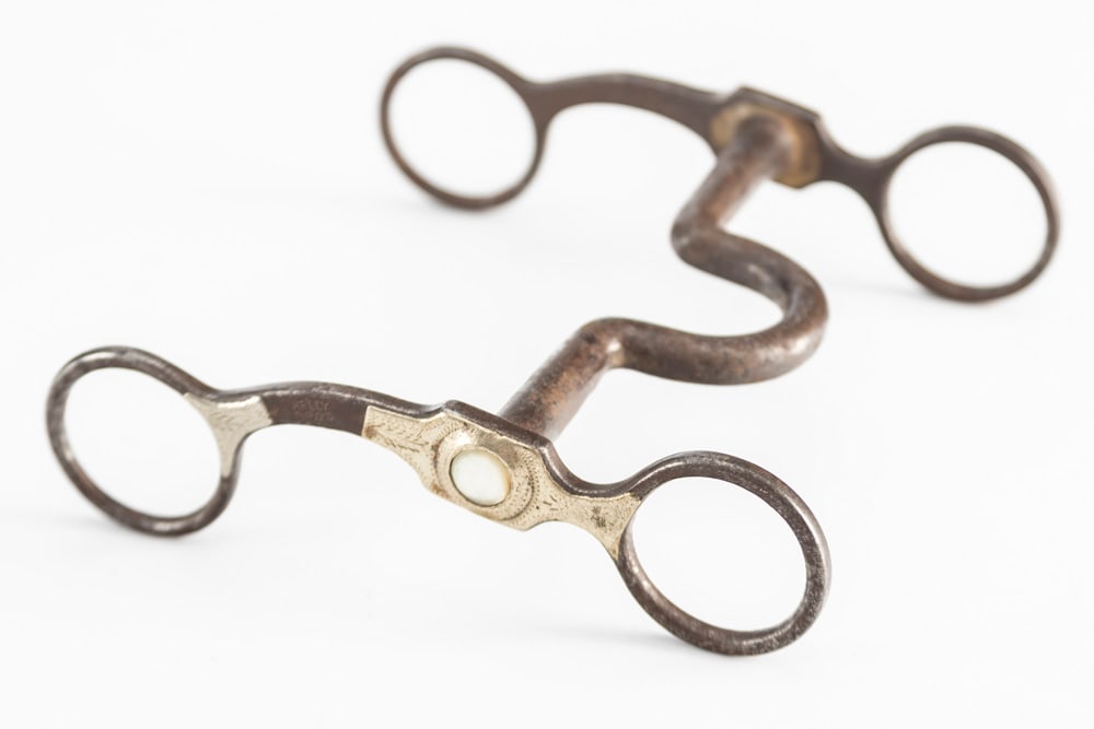 "Kelly Bros." marked silver mounted, engraved iron Bit with mother of pearl inlaid on cheek piece.: "Kelly Bros." marked silver mounted, engraved iron Bit with mother of pearl inlaid on cheek piece. Well-marked, small piece of silver missing on right side of bit. THE LATE OTIS HIBLER ESTATE.