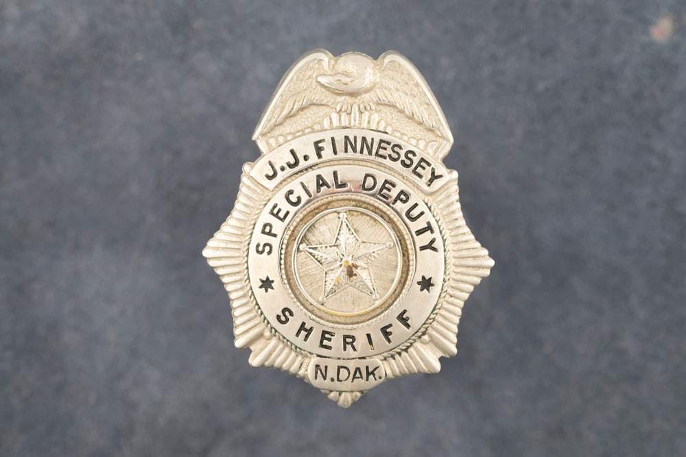 Small Shield shaped silver tone Badge with Eagle Crest marked "J.J. FINNESSEY/ SPECIAL DEPUTY/: Small Shield shaped silver tone Badge with Eagle Crest marked "J.J. FINNESSEY/ SPECIAL DEPUTY/ SHERIFF/ N. DAK.” with raised 5-point star in center. Measures 1 ½” T x 1 1/8” W