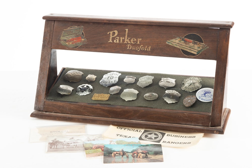 This lot consists of a total of 19 Items to include a collection of Fifteen (15) Badges, One (1): This lot consists of a total of 19 Items to include a collection of Fifteen (15) Badges, One (1) Vehicle Placard, Four (4) Postcards, and One (1) paper Wanted Poster: (1) Silver tone Circle Badge with