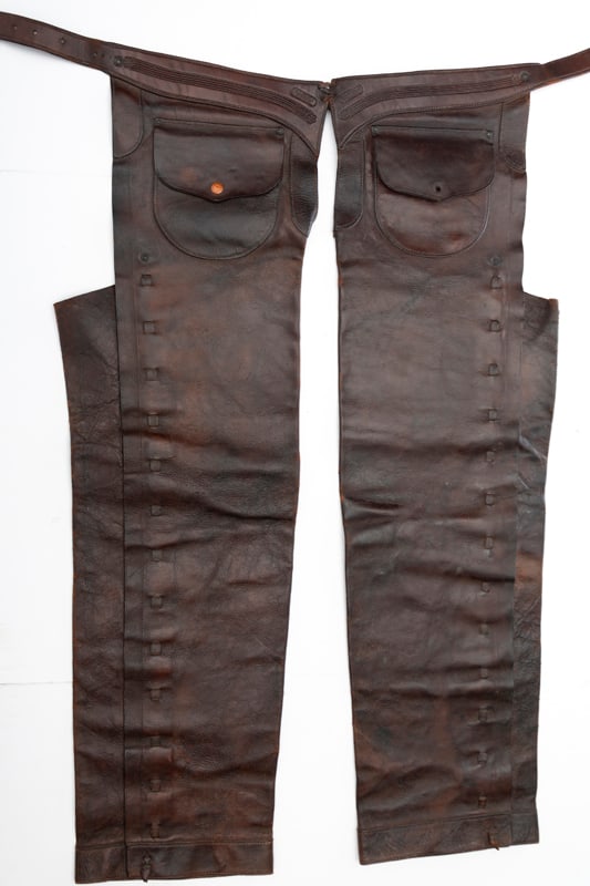 A pair of vintage "F.A. Meanea, Cheyenne" marked leather Stove Pipe Chaps with leather laced border: A pair of vintage "F.A. Meanea, Cheyenne" marked leather Stove Pipe Chaps with leather laced border and outside pockets with flaps, missing one button, approximately 40" long, "29" stamped on belt. Le
