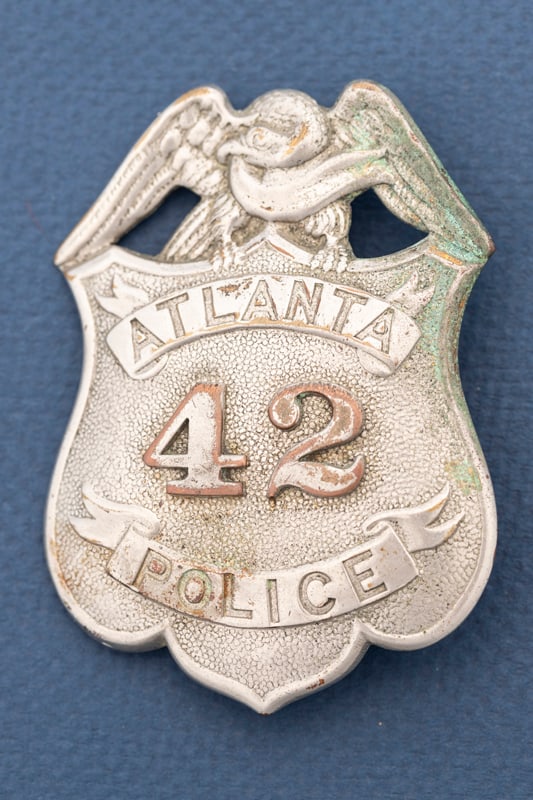 Vintage Shield Badge with eagle crest marked "Atlanta / 42 / Police", has plating loss, verdigris: Vintage Shield Badge with eagle crest marked "Atlanta / 42 / Police", has plating loss, verdigris and loss of detail due to age. Measures 3" T x 2 1/4" W, with saddle pin and catch. Estimate $325/550.