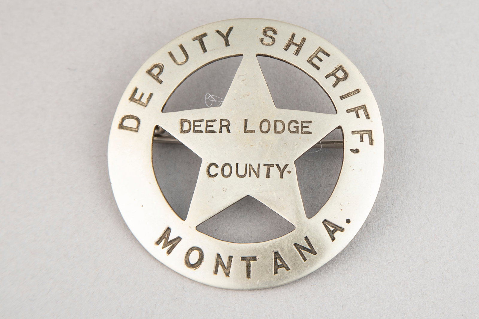 Vintage Circle Star Badge, 5-point cut out star, marked "Deputy Sheriff/Deer Lodge County/Montana".: Vintage Circle Star Badge, 5-point cut out star, marked "Deputy Sheriff/Deer Lodge County/Montana". Nice patina front and back, measures 2 1/4" D and has a heavy saddle pin and catch. Estimate $500-75