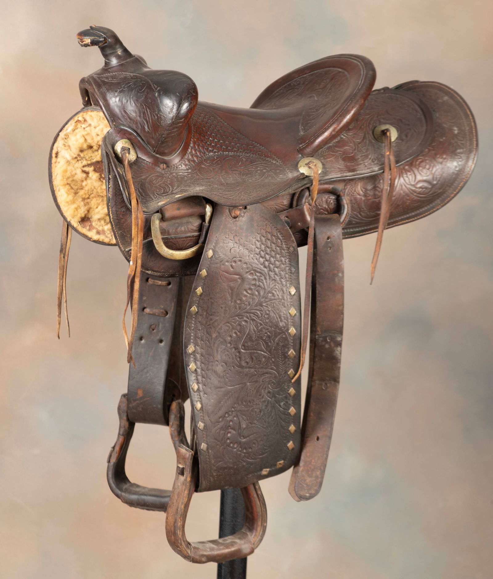 Vintage tooled leather Saddle marked "F. Vela, Floresville, Tex.", border showing nickel covered: Vintage tooled leather Saddle marked "F. Vela, Floresville, Tex.", border showing nickel covered brass diamonds, 13" seat, 2 1/2" cantle, complete with leather wrapped wooden stirrups. Grant Teaff Col