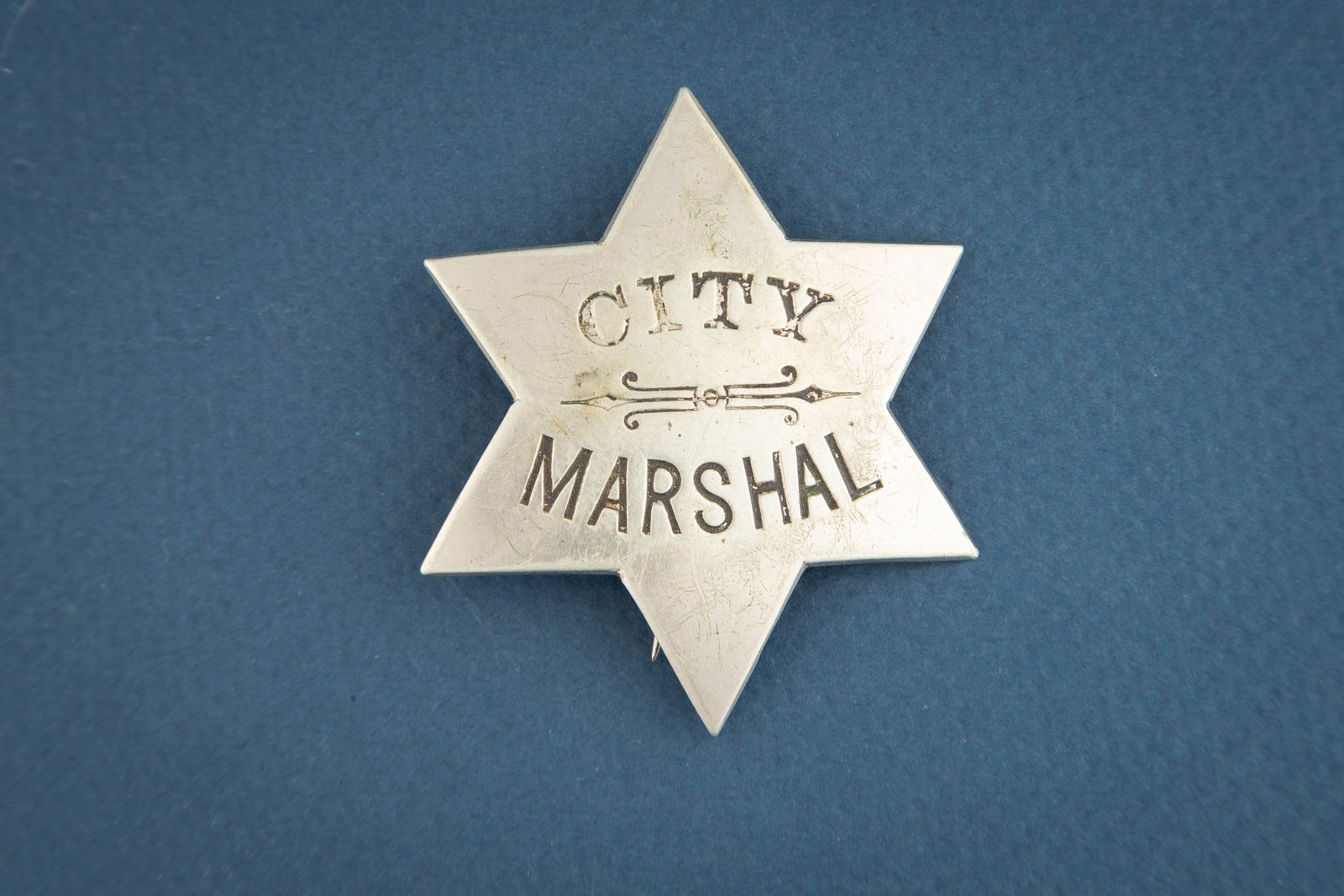 Vintage silver tone 6-point Star Badge marked “CITY/MARSHAL??, great patina and wear with some: Vintage silver tone 6-point Star Badge marked “CITY/MARSHAL”, great patina and wear with some black enamel loss, no hallmark, has saddle pin and catch. Estimate $300-500. Lee Hutcheson Collect
