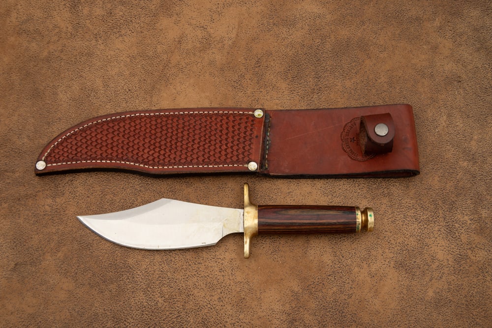 Handmade Clip Point Bowie Knife in leather sheath, appears to have a rosewood handle, heavy brass: Handmade Clip Point Bowie Knife in leather sheath, appears to have a rosewood handle, heavy brass cross guard and brass pommel with 6 1/4" blade, 11" overall. Maker mark not visible. Sold with leather