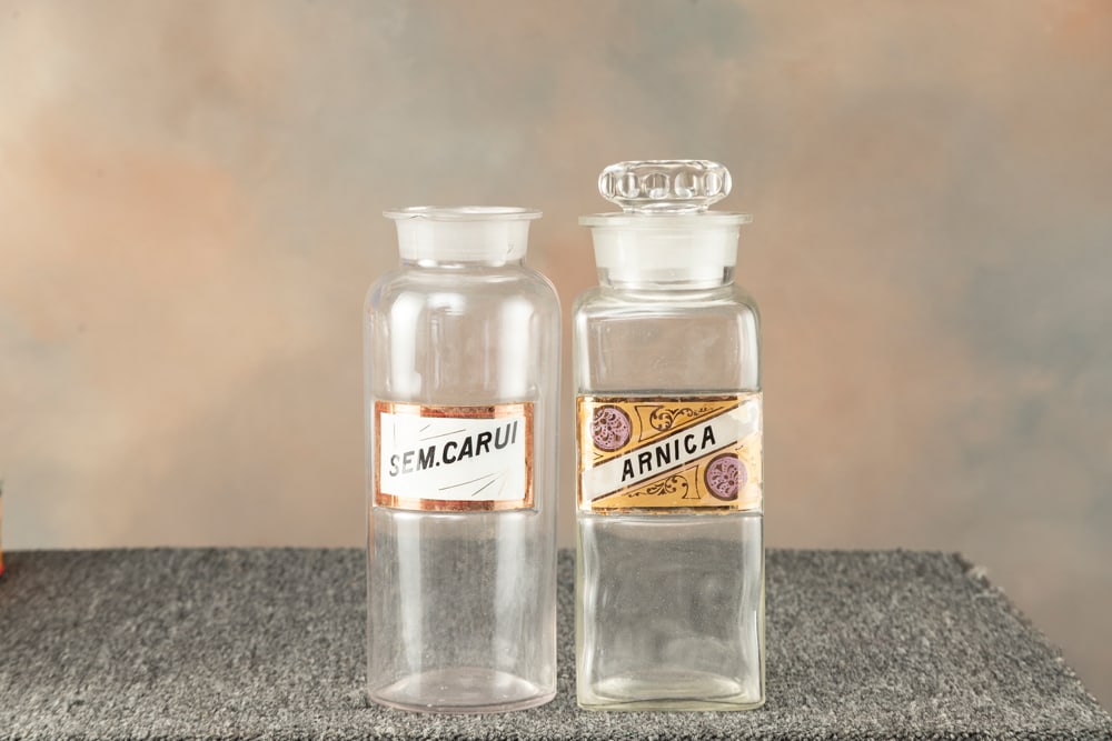 Two antique Apothecary Jars. Both have porcelain and glass labels. One has ground stopper. One: Two antique Apothecary Jars. Both have porcelain and glass labels. One has ground stopper. One advertises "SEM.CARUI", 10 3/4" T with 4" round base. The other advertises "ARNICA". measures 10 3/4" T w
