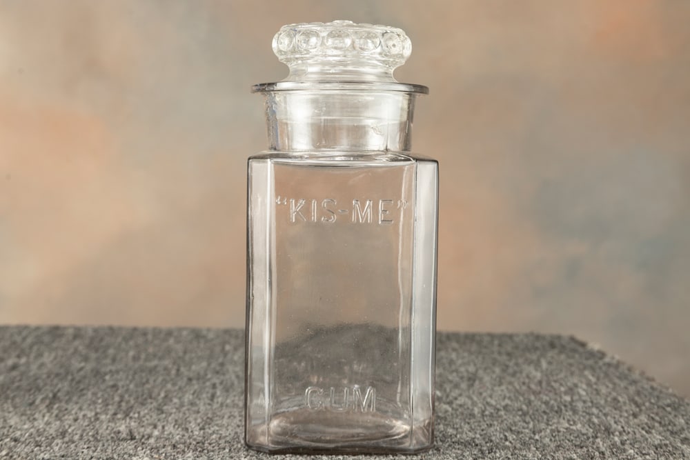 Antique Advertising Jar for "Kis-Me Gum" embossed on front panel, marked on back panel "Kis-Me Gum: Antique Advertising Jar for "Kis-Me Gum" embossed on front panel, marked on back panel "Kis-Me Gum Co., Louisville, Ky.", measures 10 1/2" T x 5" sq. with ground stopper.
