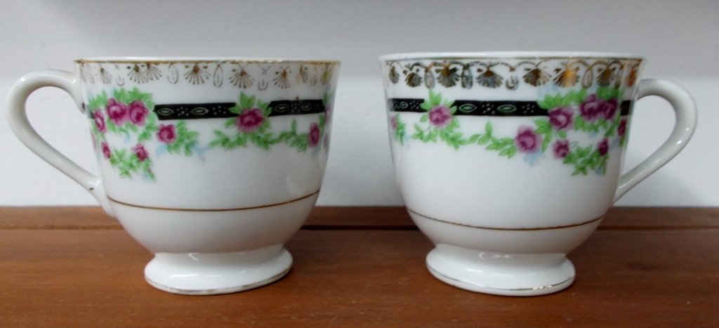 Vintage Cups: Two vintage tea cups made in Japan measuring at 2" tall. The white cups have a black line wrapping around the cup with soft red roses placed around it.