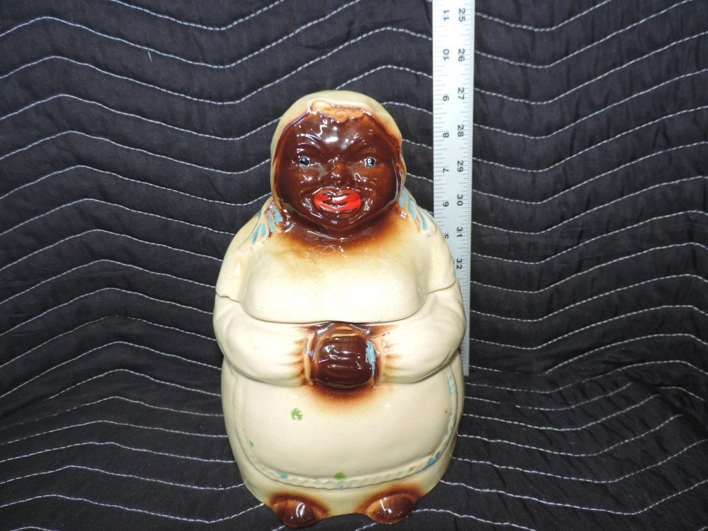 Black Americana Cookie Jar: This rare vintage cookie jar is a great piece of Black Americana. The lady has a big smile and is dressed in a cream colored dress with a blue-lined patterned apron over top. On her head she is wearin