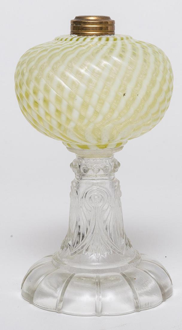 Vaseline Opalescent Swirl Oil Lamp: On mold blown font with swirled ribs in opposite direction from opal swirl, on clear palm leaf & fan pattern column on domed & lobbed foot, brass collar, 5" diameter x 8 1/2" high.