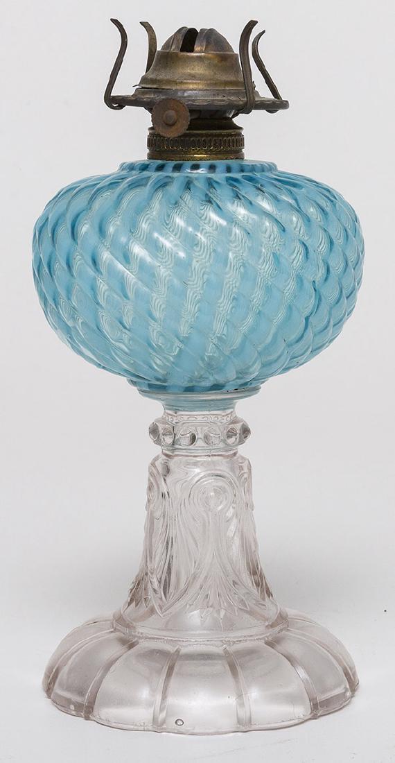 Blue Opalescent Oil Lamp: On mold blown sapphire blue font with swirled ribs, and vertical white opal ribbing on clear palm leaf & fan pattern column on domed & lobbed foot, brass collar, 5" diameter x 8 1/2" high.