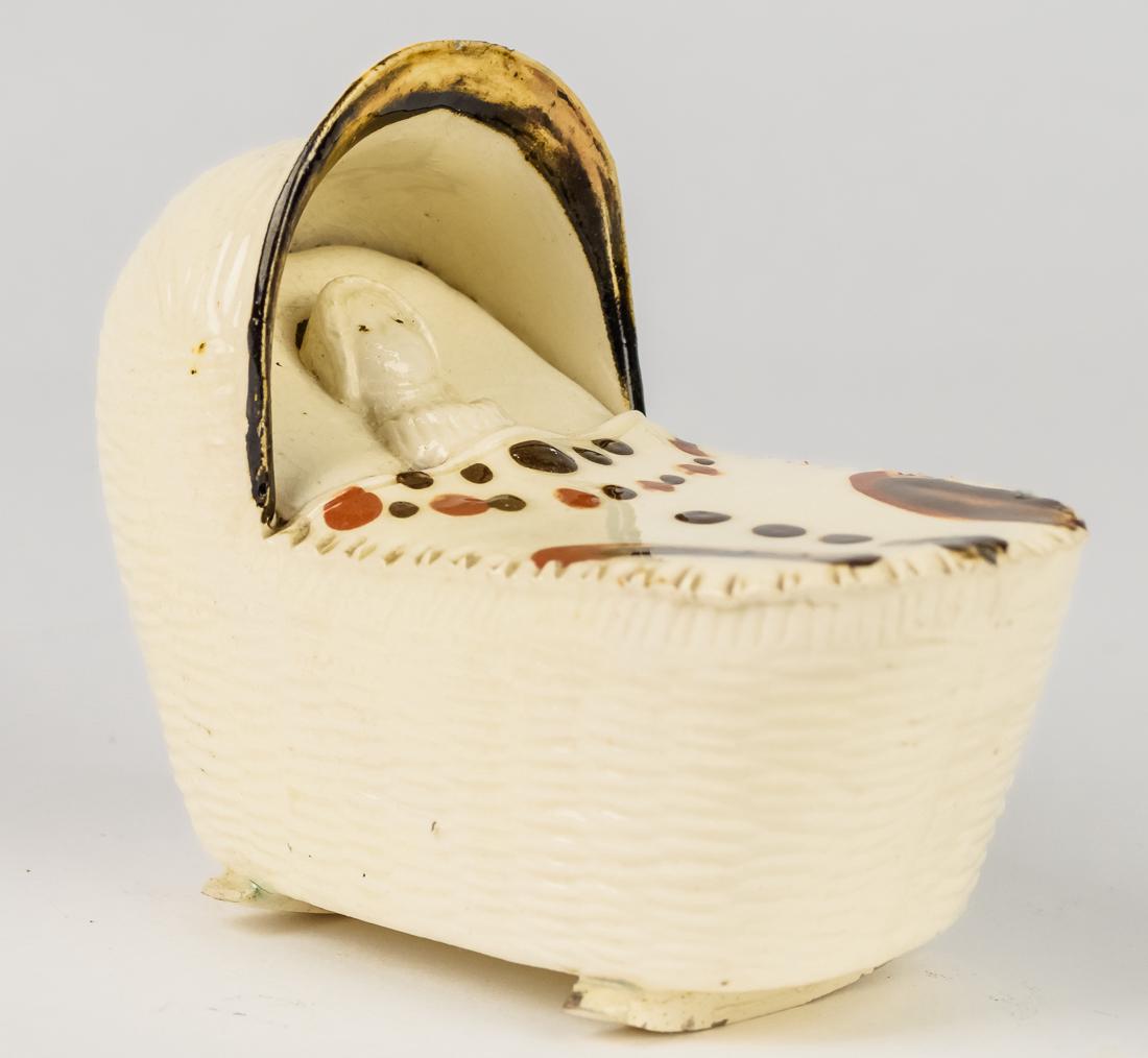 Early Staffordshire Child in Cradle: Circa 1790-1800 in creamware with hand painted decoration on blanket covering child on its back, wicker rocking cradle. 4 1/2" x 2 1/4" x 3 3/4" high.