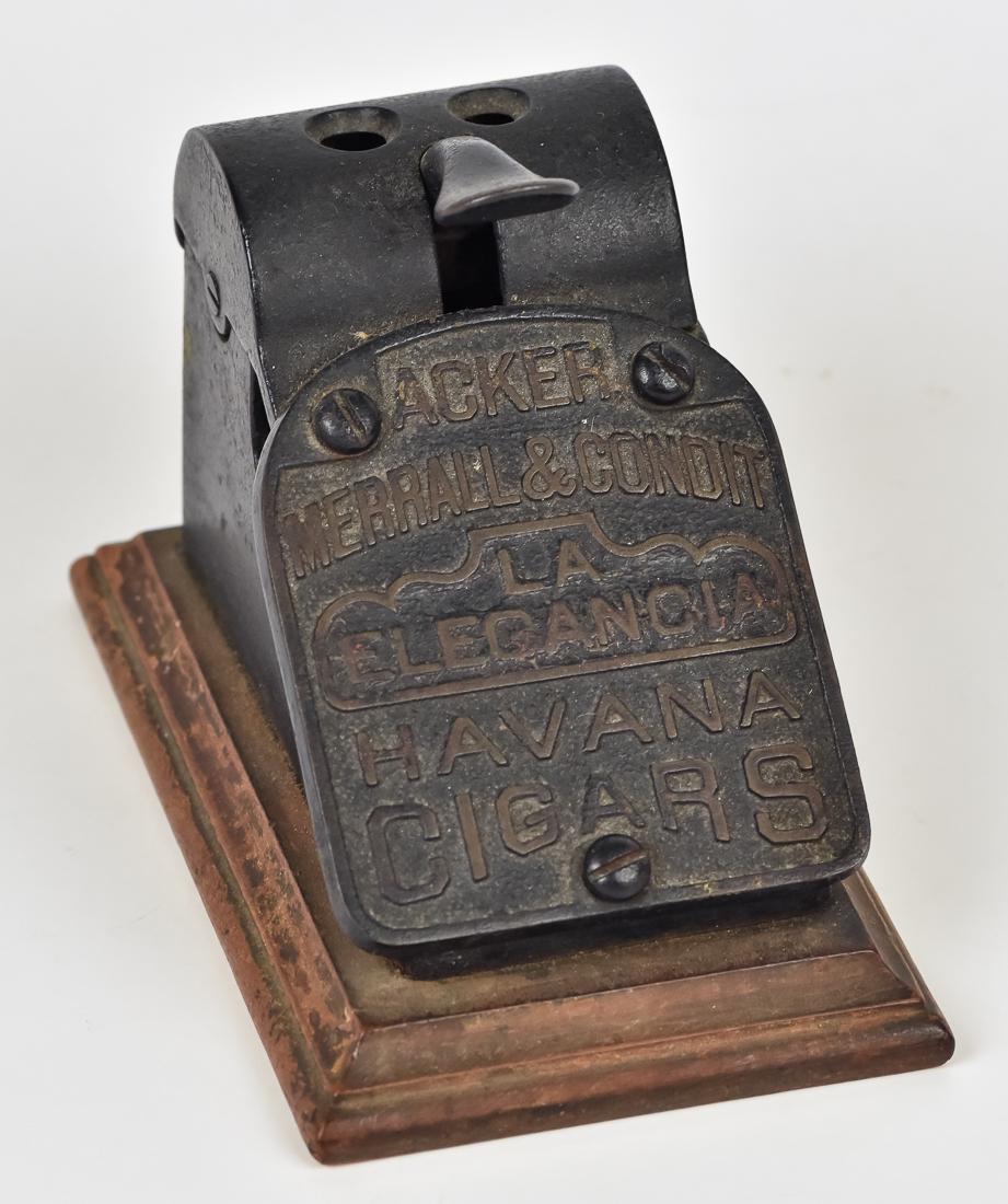 Advertising Cigar Cutter: Desk or bar top model in cast iron with raised text on front reading Acker/Merrall & Condit/La/Elegancia/Havana/Cigars, with stepped wood base in old red washed finish and two different sized holes at