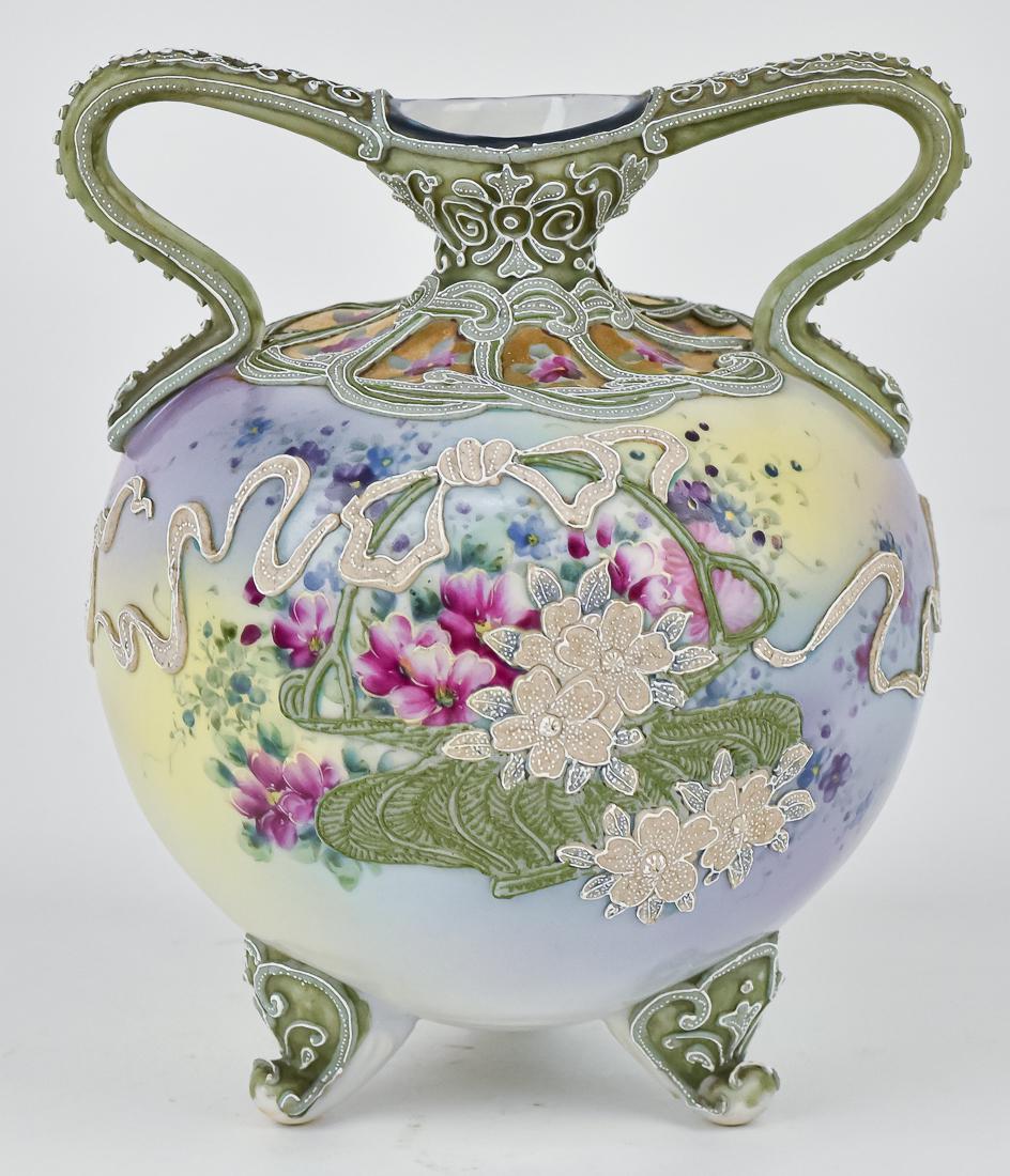 Nippon Vase with Moriage Decoration: Double handled with green moriage basket and white moriage florals on front, and the white continuing to the back of the vase. Maple leaf backstamp. 7 " high. One tiny bead missing on handle, otherwis