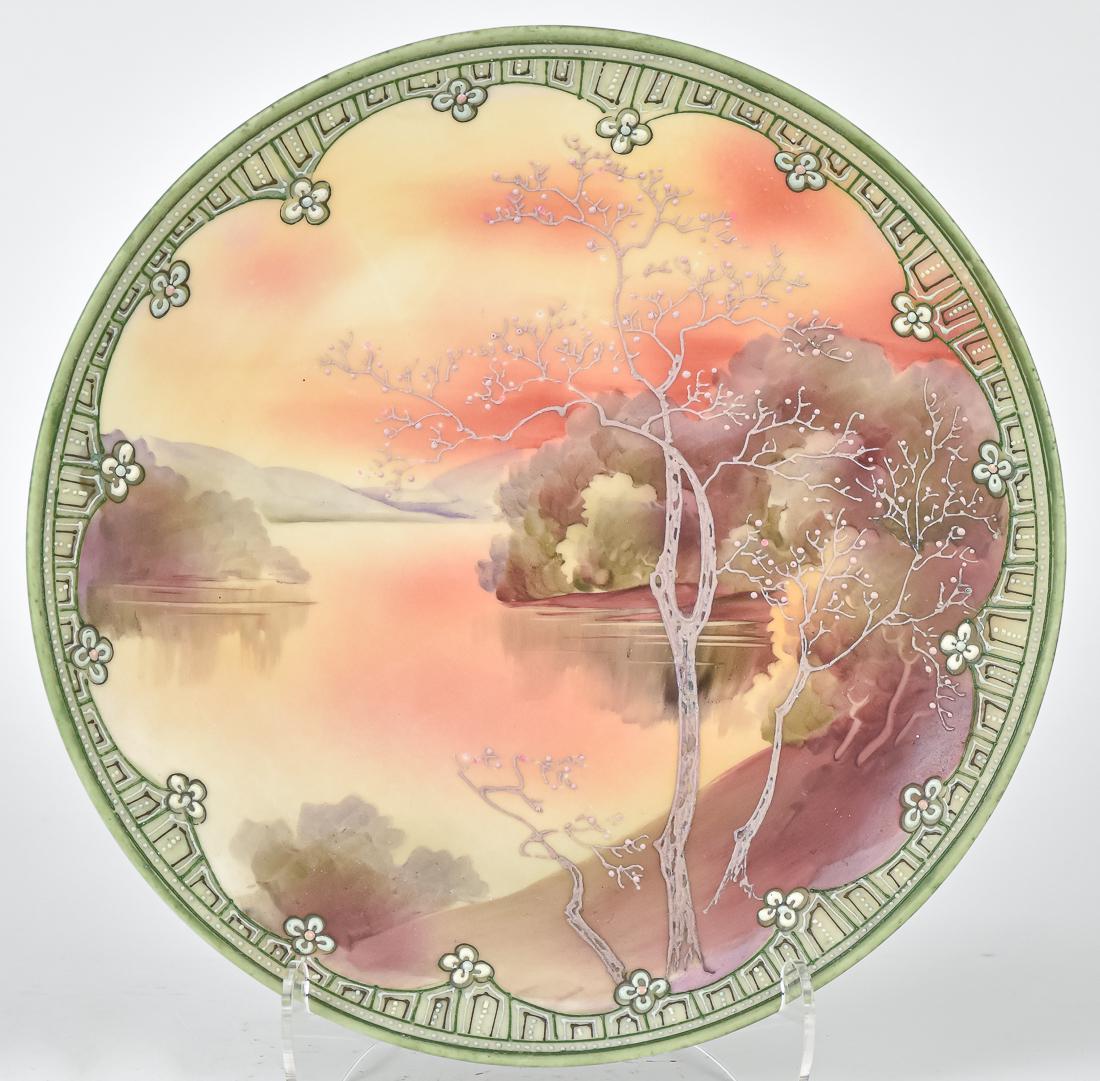 Nippon "Galle" Scenic Hanging Plaque: With hand painted lake scene, surrounded by raised floral decoration. Maple leaf Nippon backstamp. 10" diameter. Good condition.