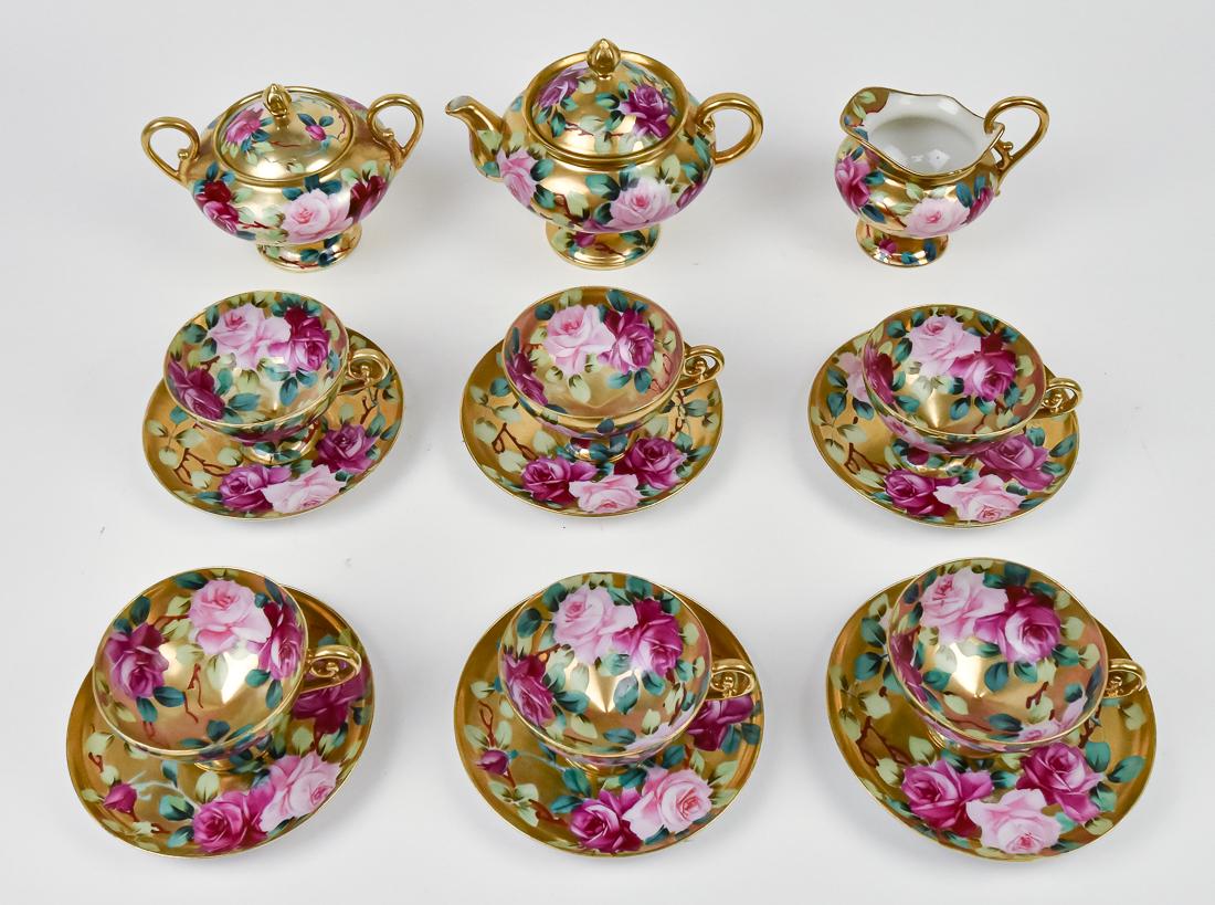 Nippon 9 Piece Tea Set: With rose and bright gold decoration, consisting of teapot, creamer, sugar, and 6 footed cups & saucers. Maple leaf backstamp. Teapot, 6" High X 7 1/2" Wide. Good condition.