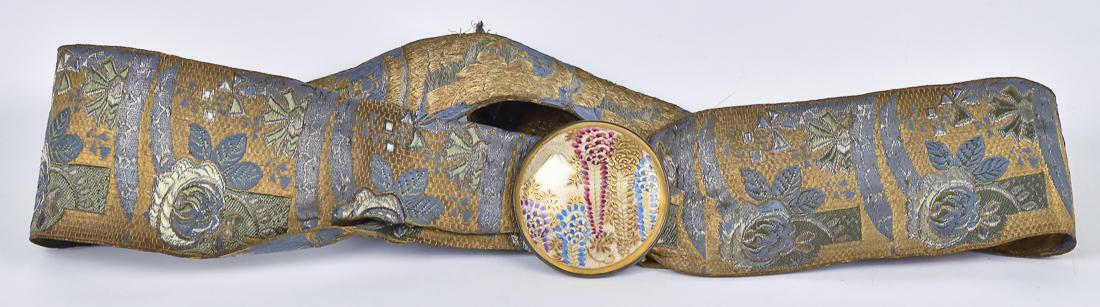 Japanese Silk Belt with Satsuma Buckle: Polychrome woven silk belt with floral decoration in blue, green, silver on gold ground with circular buckle with polychrome painting of Mount Fuji, 2" diameter, mounted on silver plated back, total l