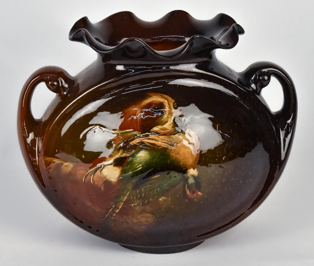 Rozane Ware Vase with Dog: Hand painted with retreaver with pheasant in mouth, pillow vase with two scroll handles and ruffled lip. Raised stamp mark on base. Signed with artist initals by tail of bird, H.?. 5 3/4 x 11 x 9 1/4"