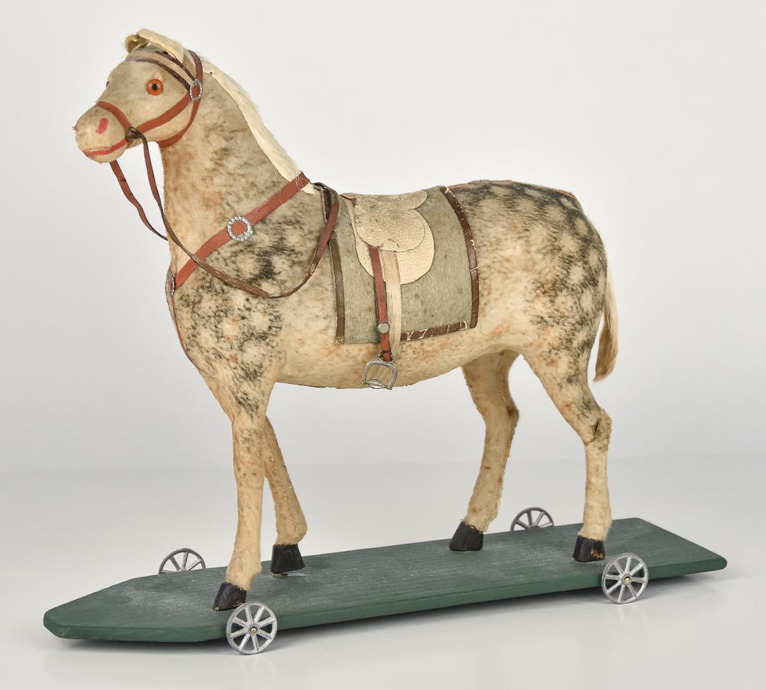 Early German Horse Pull Toy: Mid 19th century, unmarked felt over wood and paiper-mache, on green painted wood base with four cast pewter wheels, ivory colored leather saddle with blue felt blanket with gold trim fax leather brid