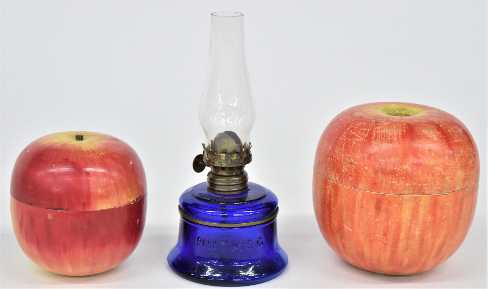 Nutmeg Lamp & Two Apple Caddies: Lot of three including a cobalt blue miniature marked Nutmeg oil lamp with original brass burner and chimney, 3" diameter x 6 1/2" high; plus two turned wood apple form caddies in original painted fin