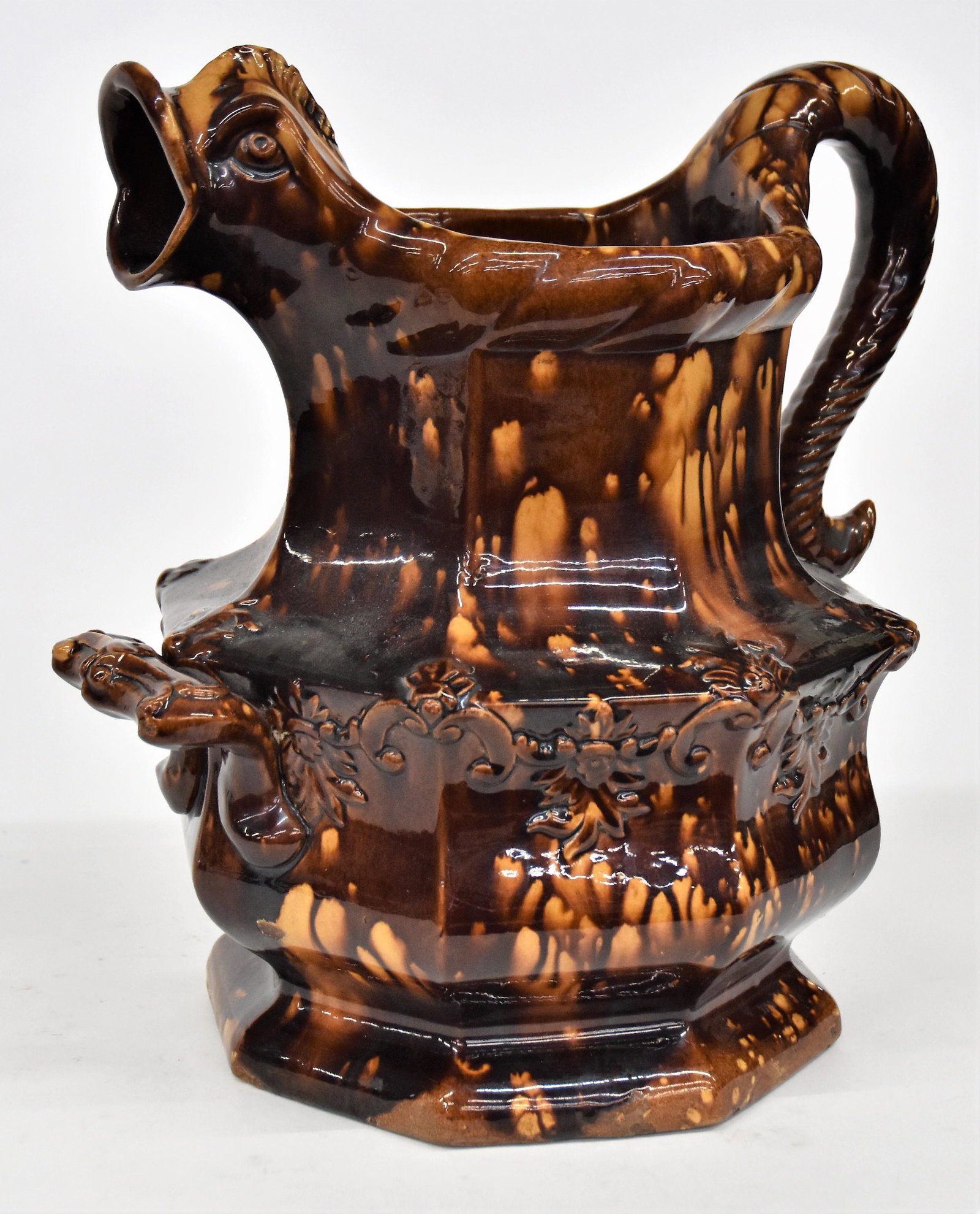 Large Store Display Figural Benn/Rockingham Pitcher: Massive form with dolphin spout and roped C form handle with additional handle below spout, roped rim, octagonal with relief scroll work, 14 x 12 x 13 1/2" high. Condition Fine.