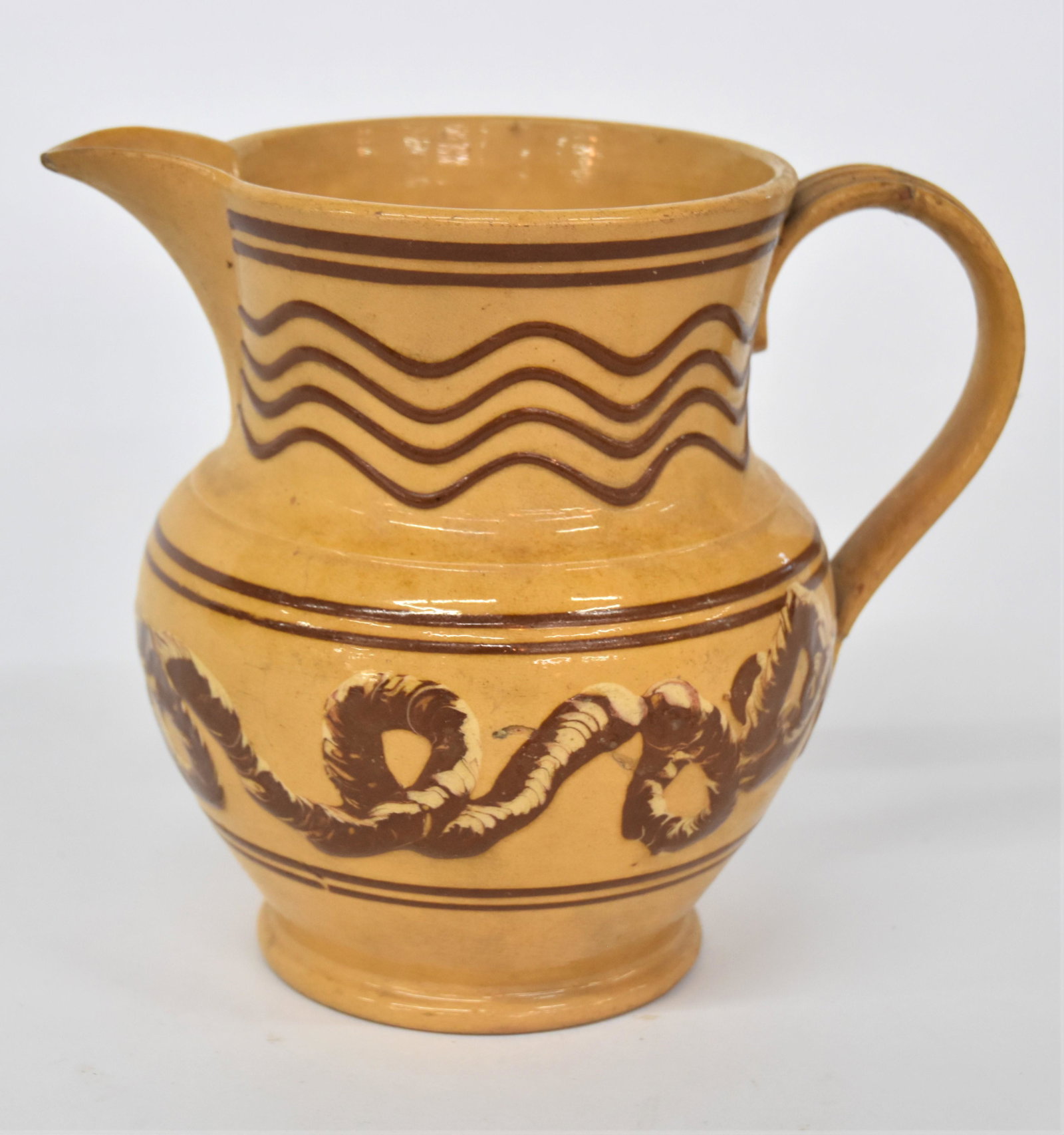 Outstanding Cincinnati Decorated Yelloware Pitcher: Attributed to Wm. Bromley made during the early period when his kiln was in Cincinnati. This English form pitcher has classic bulbous form with applied reeded strap handle, decorated with two brown sl