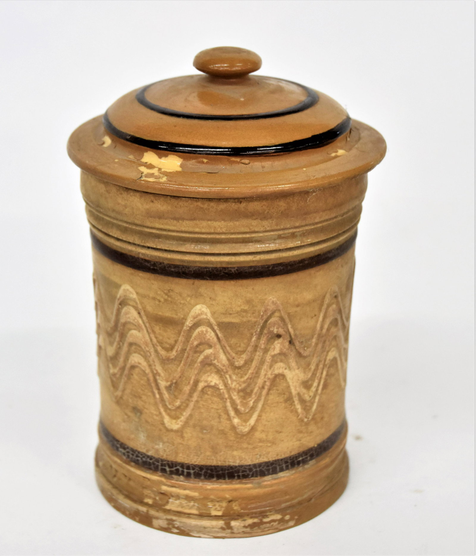East Liverpool, Ohio Yelloware Tobacco Jar: Unsigned, decorated with brown annular banding and white wavy four line slip trailed banding on cream ground, domed lid, 5" diameter x 7 1/2" high. Condition older professional repair to lid and base,