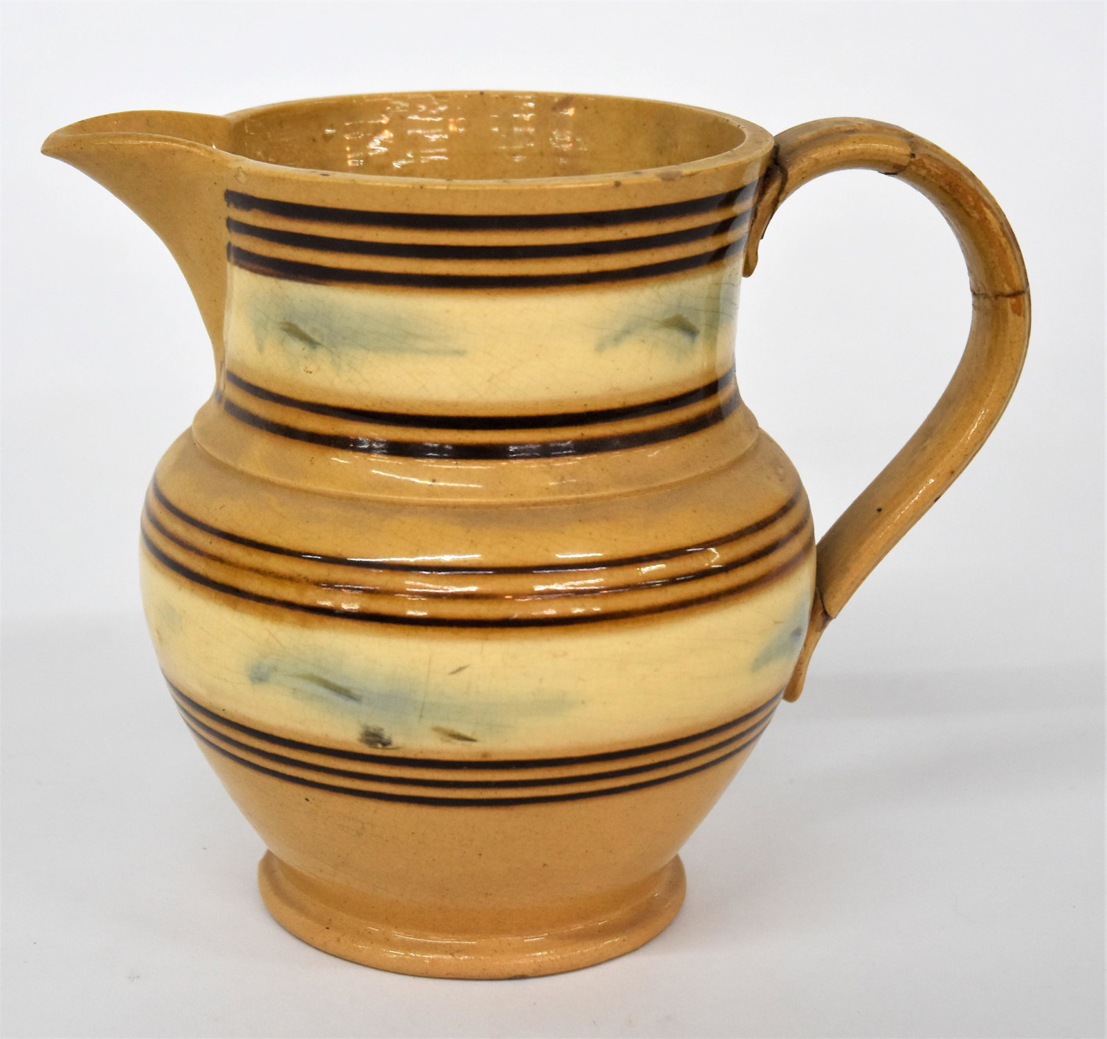 Cincinnati Decorated Yelloware Pitcher: Attributed to Wm. Bromley's Cincinnati kiln, circa 1850's, classic bulbous English form with applied C form handle, neck decorated with cream colored band with blue dendritic (sea weed) pattern, flake