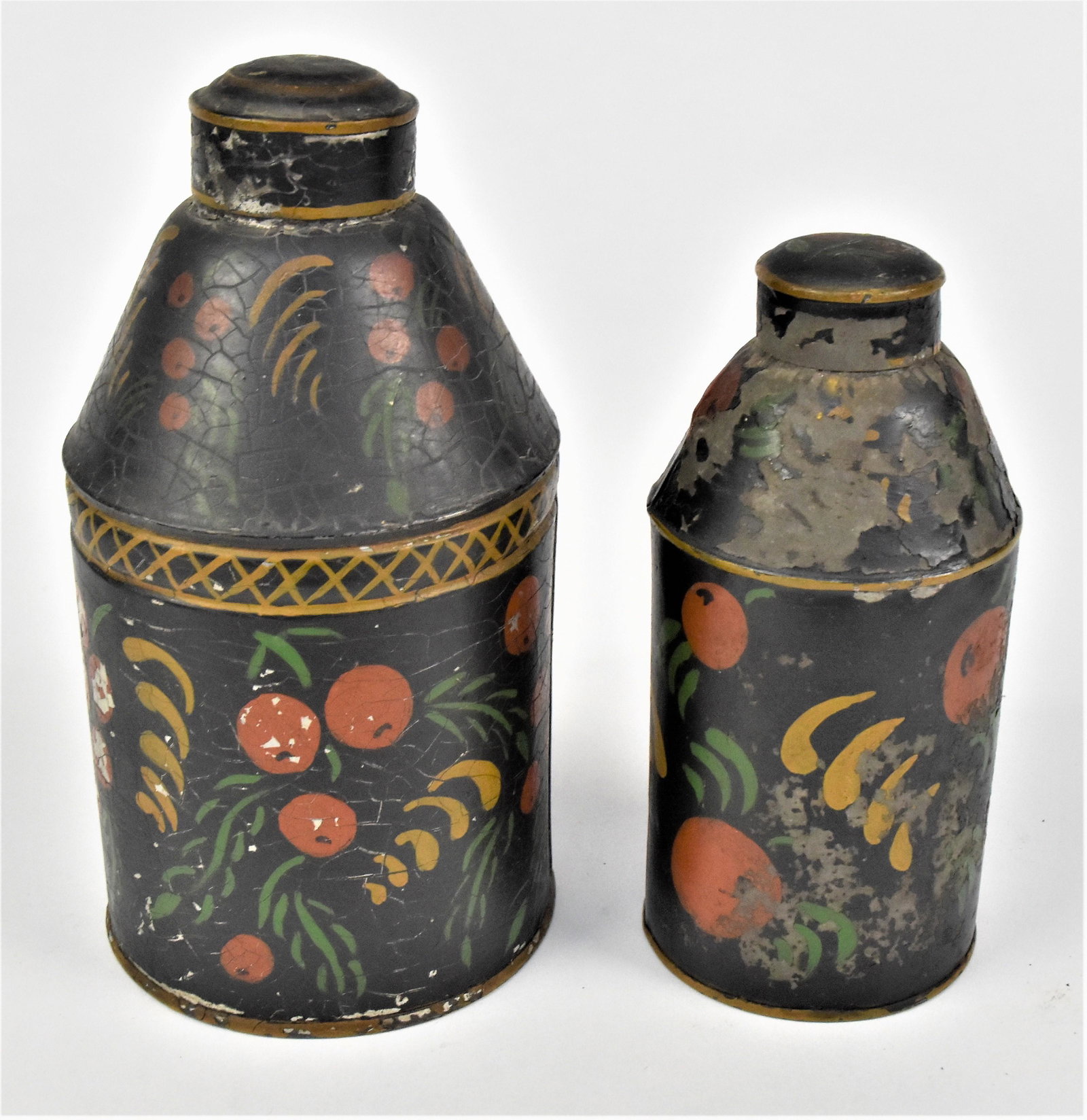 Two Toleware Tin Caddies: Both in original polychrome painted finish with fruit and leaves on black grounds, friction fitted domed lids, 4 1/3 x 8 & 3 1/8 x 6 3/4" high. Condition Paint on 1st circa 89%; 2nd paint 75%.