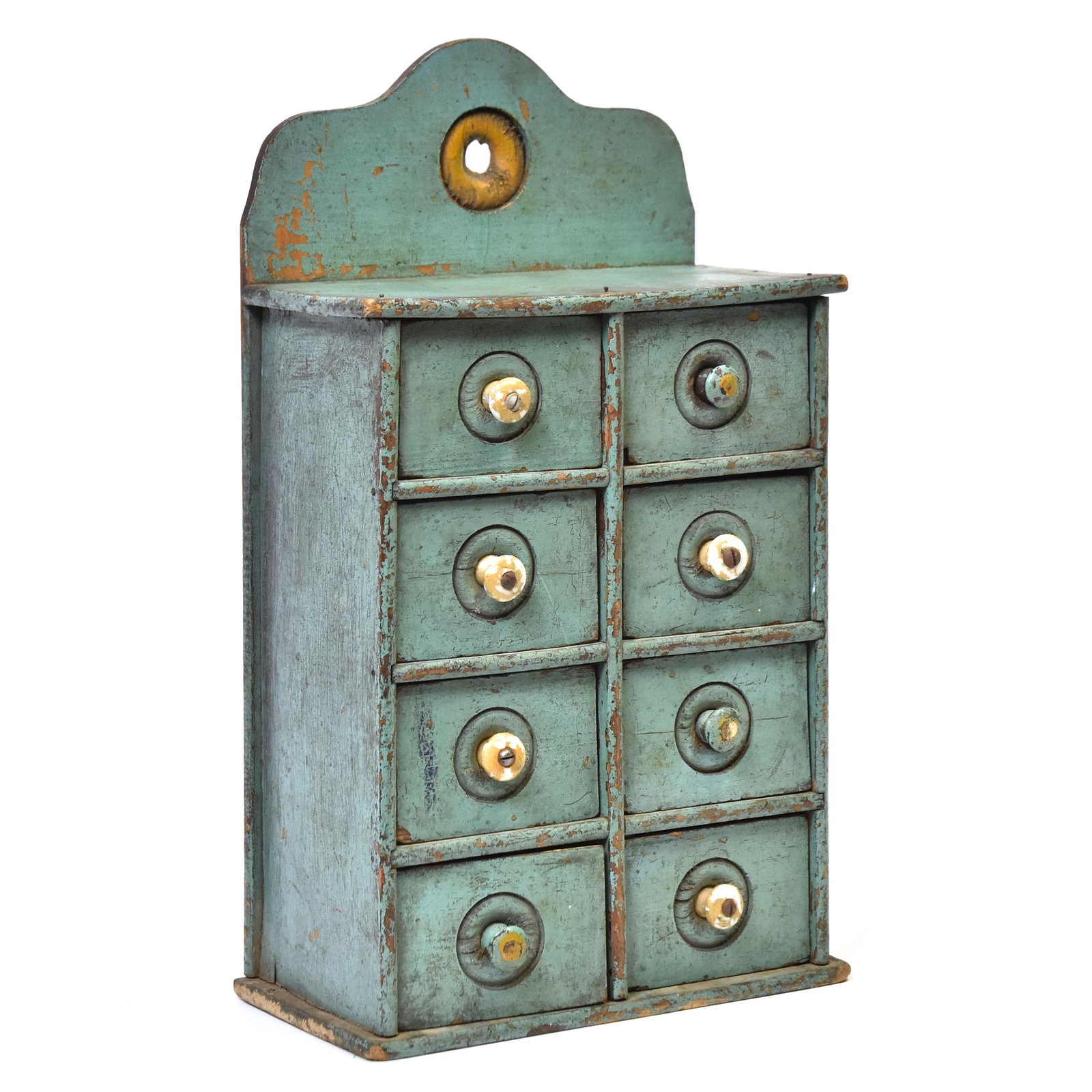 Hanging Spice Rack in Old Paint: Maple with tombstone crest with bulls-eye hanger and drawer fronts, 8 drawers with original porcelain knobs, all in period turquoise painted finish, circa 1890, 5 x 9 1/2 x 17" high. Condition paint c