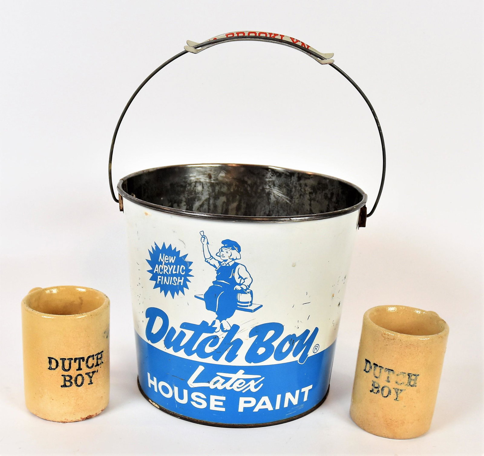 Dutch Boy Bucket & Mugs: Lot of three including chromolithographed tin paint bucket with wire swing bale handle with snap on tin grip9 1/2" diameter x 8 1/4" high; and two yelloware pottery coffee mugs with blue Dutch Boy on 