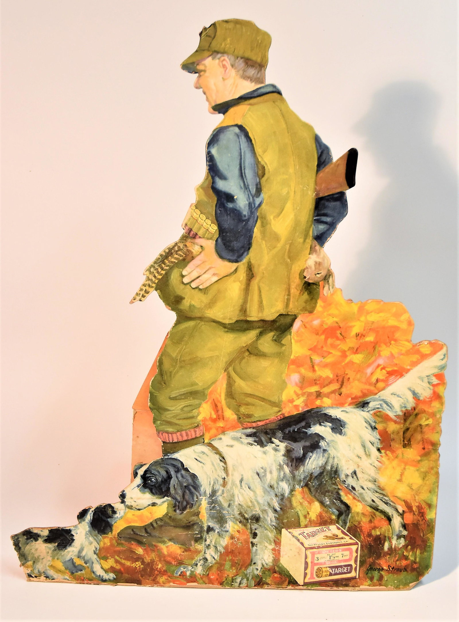 Peters Shells Card Stock Display: Chromolithographed cut-out on heavy card stock hunter walking with shotgun in fall landscape with pointed and puppy, bird in left pouch pocket of vest and rabbit in right, box of Peters Target 12 ga. 