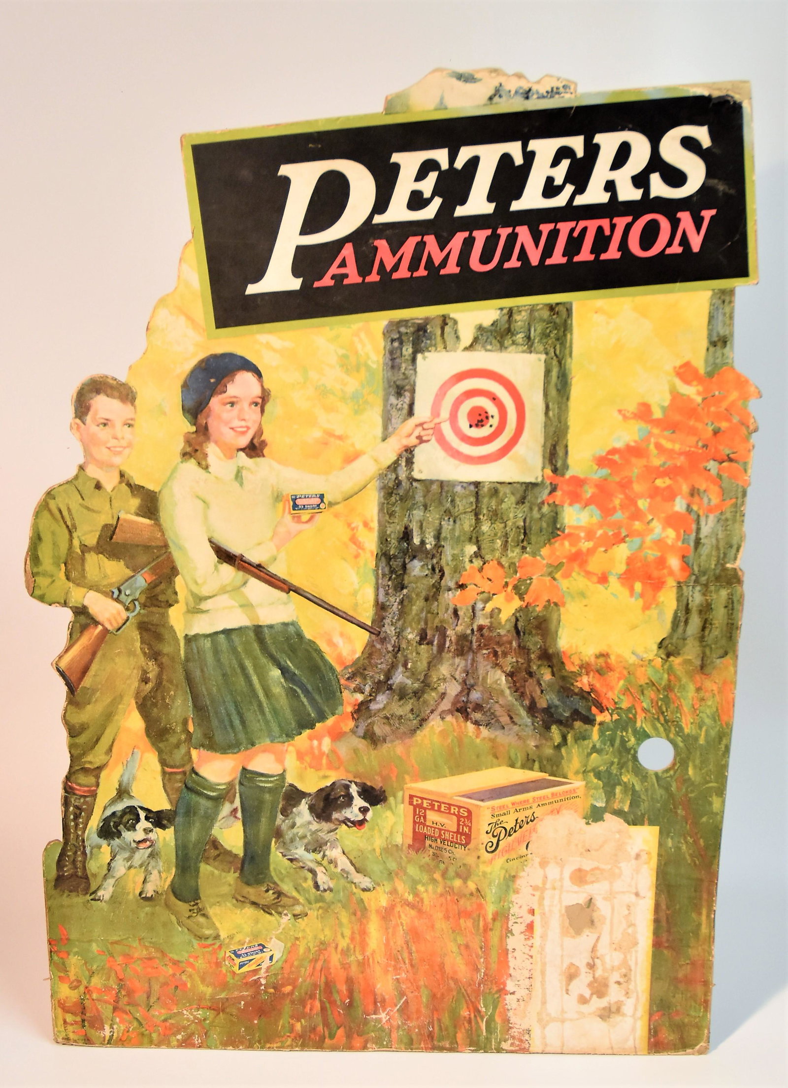 Peters Shells Card Stock Display: Chromolitographed showing young teen boy and girl target shooting with target on tree and Peters Ammunition above, girl holding box of .22 short with open wood crate of Peters 12 ga. On ground and two