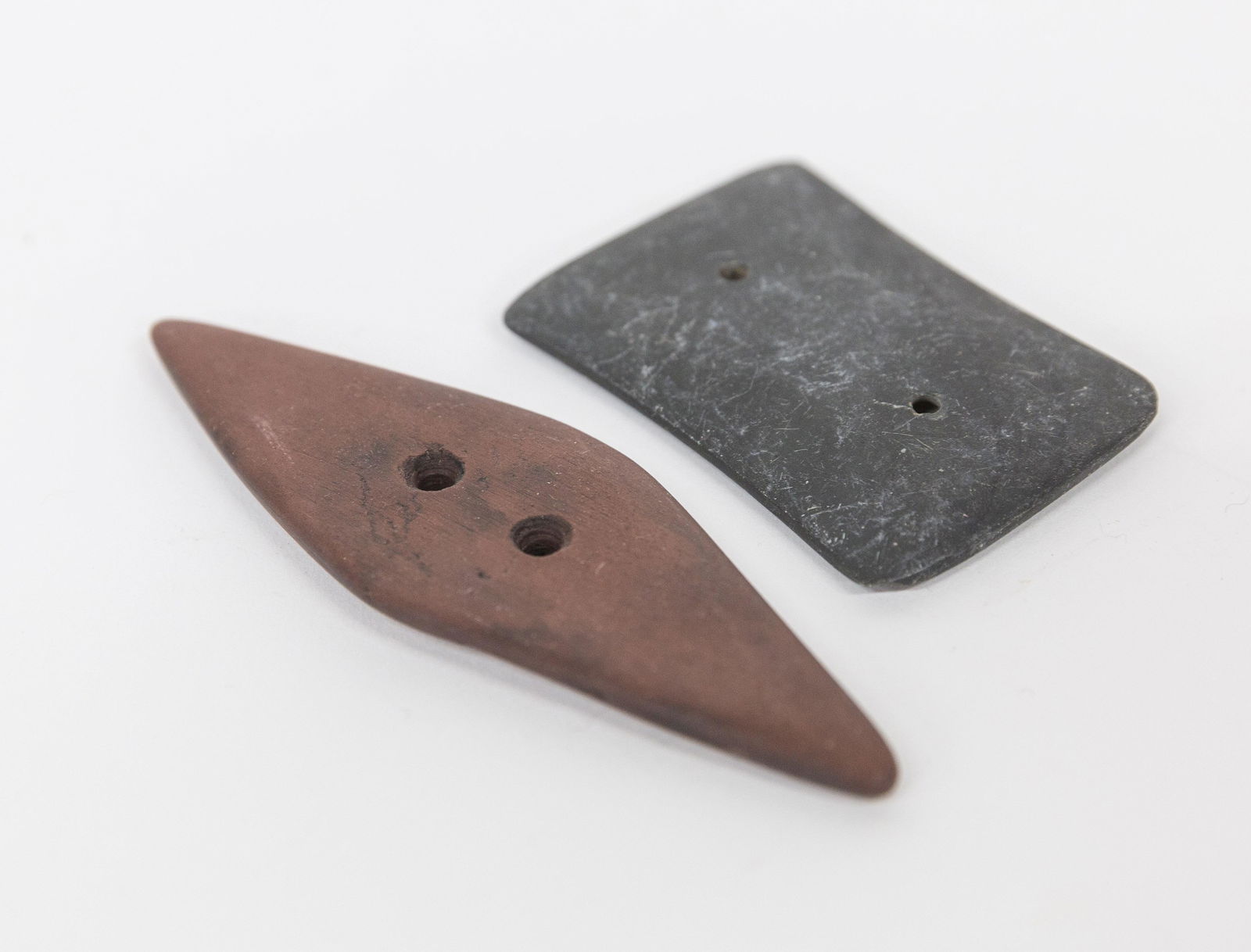 Two Native American Slate Gorgets: Including a bi-pointed example in red slate, 4 3/8" long x 1 5/8" wide; and gray slate with concave sides and convex ends, 2 1/2" long x 1 3/4" wide, each with double drilled holes, drilled from both