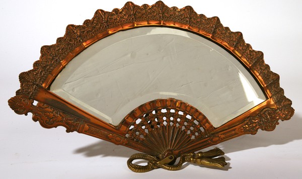 EDWARDIAN FIGURAL BRASS DRESSER MIRROR: In the form of a Victorian ladies hand fan, in copper finish with beveled mirror and brass kickstand back. 18.5" x 10.5" high.
