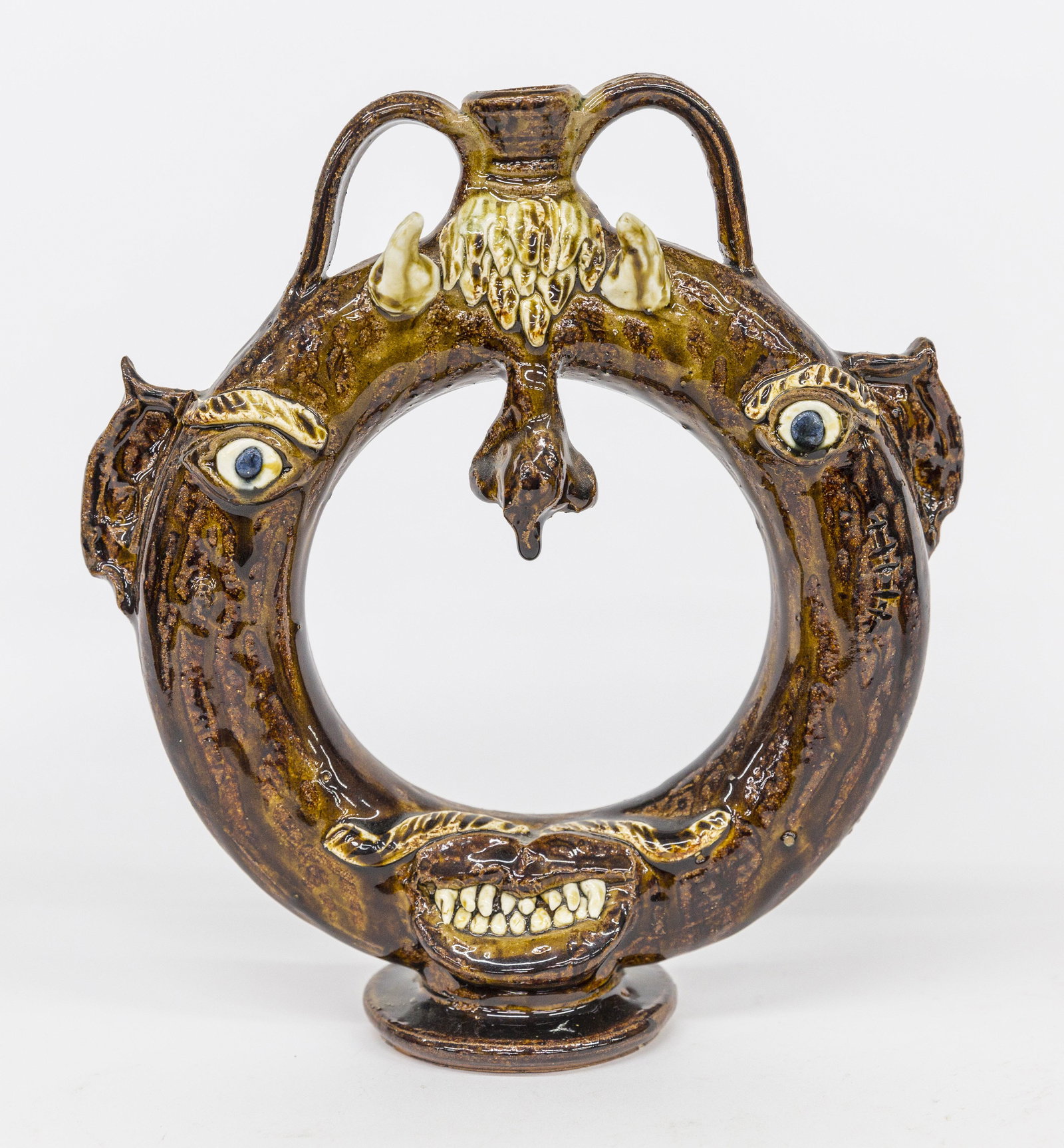 Albert Hodge Harvest Ring Flask: Brown alkaline glaze, Devils face type in ring form flask with applied porcelain horns, eyes and teeth, stamped on back & base Albert Hodge Vale N.C., 9 1/2 x 1/2 x 10 1/2" high. Condition Fine.