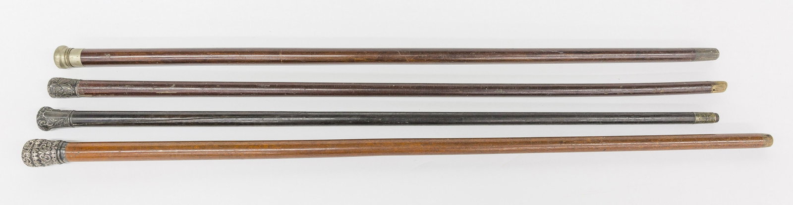 Three Silver Knob Walking Sticks Plus: Lot of four including three with unmarked Sterling or coin silver knobs, floral chased, including one on tapered malacca shaft, missing ferrule, total length 36"; plus one on tapered ebony shaft, with