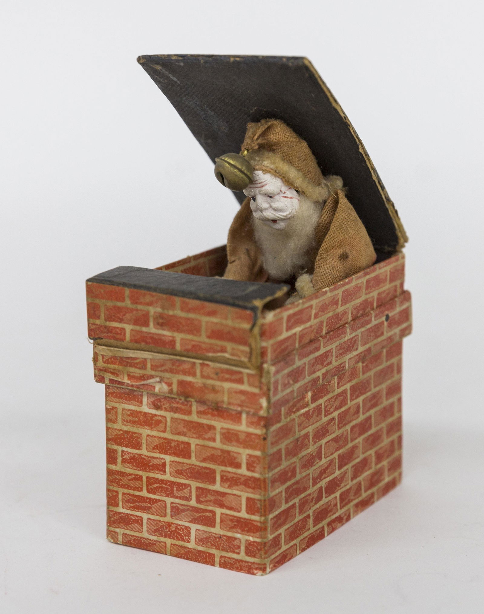 Early German Santa Jack-In-The-Box: Card stock box with printed red brick pattern as a chimney, front flap folds down and Santa with his bag pops up, composition face red & white cloth outfit with small brass hawks bell on cap end, 2 x3