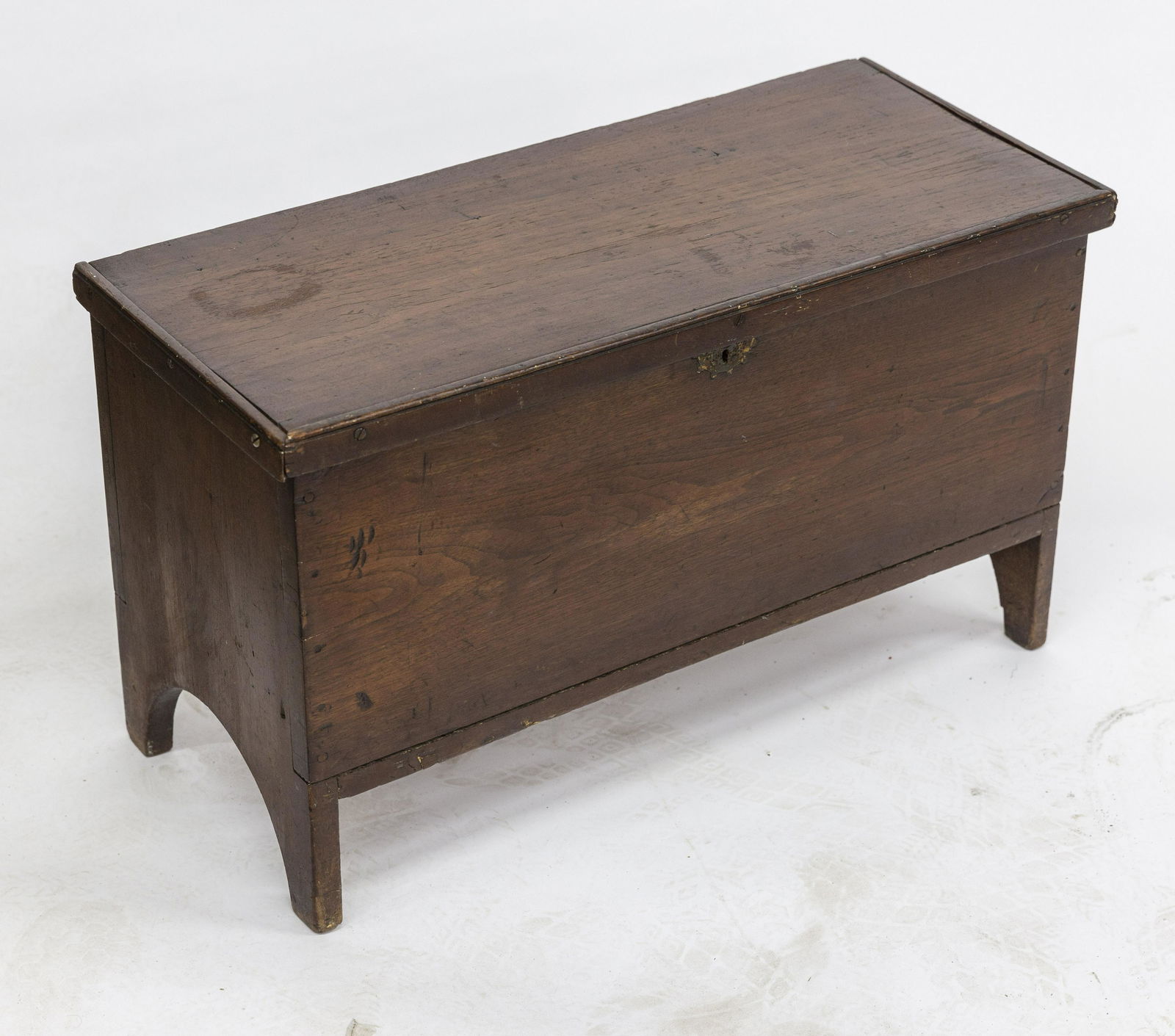 Child Size Walnut Blanket Chest: Circa 1830-50 with locking hinged lid with applied edge molding, unusual folk art dimpled brass key hole escutcheon, solid ends with arched cut-out feet, 31 x 13 1/4 x 13" high. Condition hinges reset