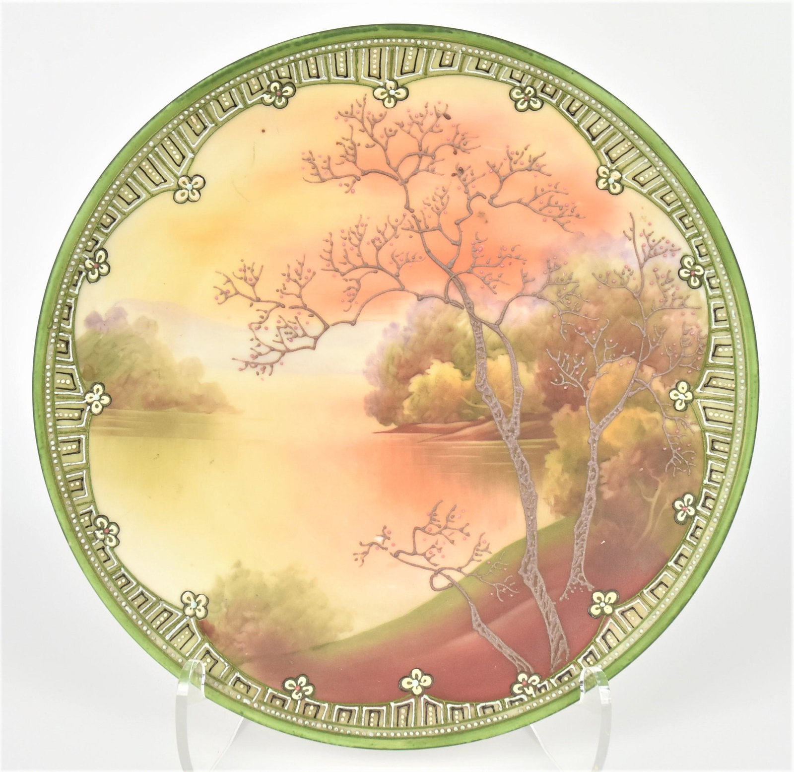 Nippon Galle-Style Scenic Plaque: Raised foreground trees overlooking a lake edged with tall foliaged trees at eventide. Decorative raised enamel border. 10" diameter. Maple leaf backstamp. Tranquil setting, good condition.