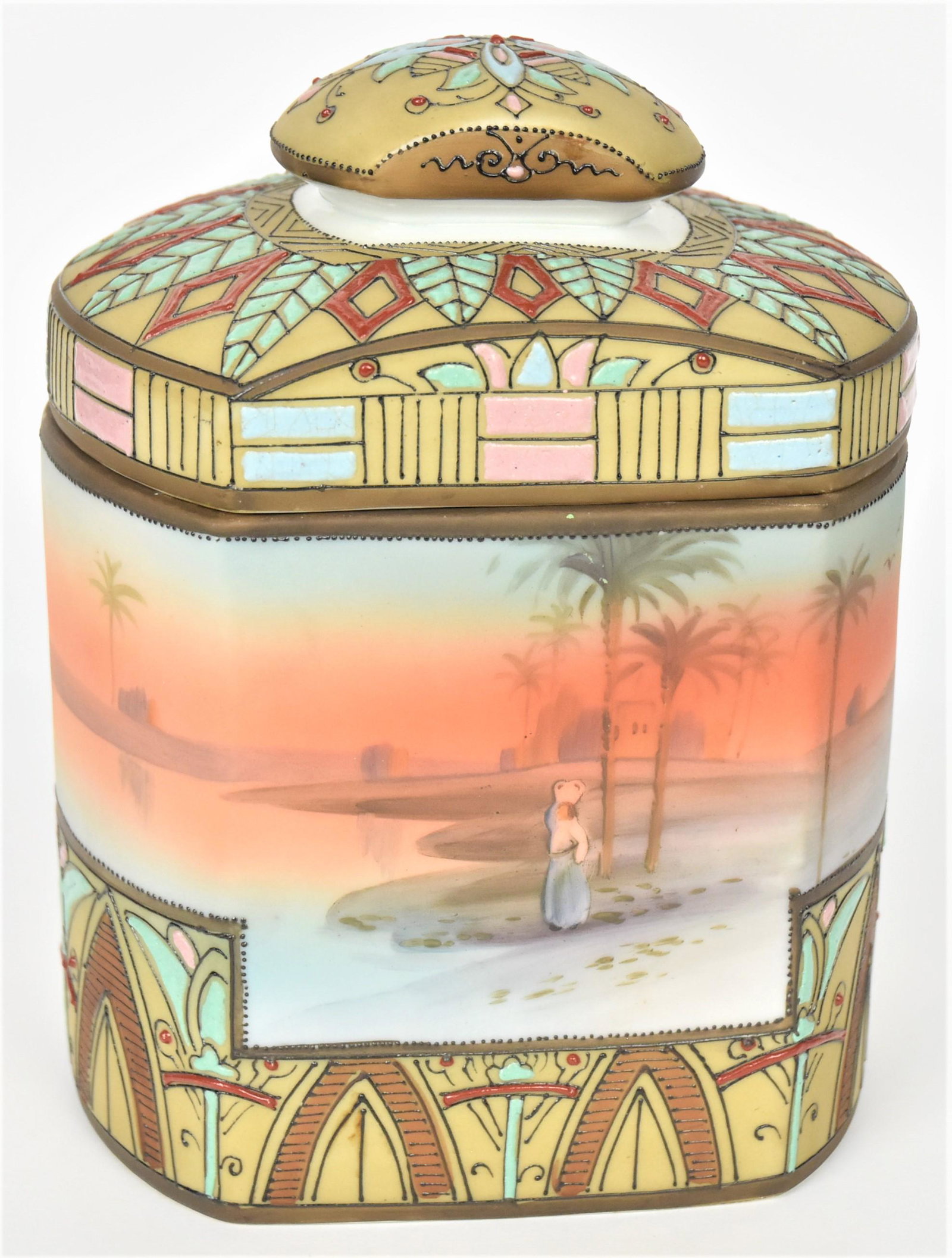 Nippon Egyption Covered Humidor: Continuous lake and palm trees at eventide with a person standing along the shore. Highly enamel designs at the cover and around the containers base. M in wreath backstamp 7"tall, 5 1/2" long, 4 1/4"w