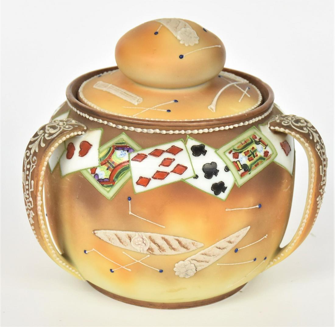 Nippon Moriage Handled Humidor: Playing cards painted on the shoulder, with matches, cigarettes and cigar in raised designs to the handles. Maple leaf backstamp. Handsome and in good condition.