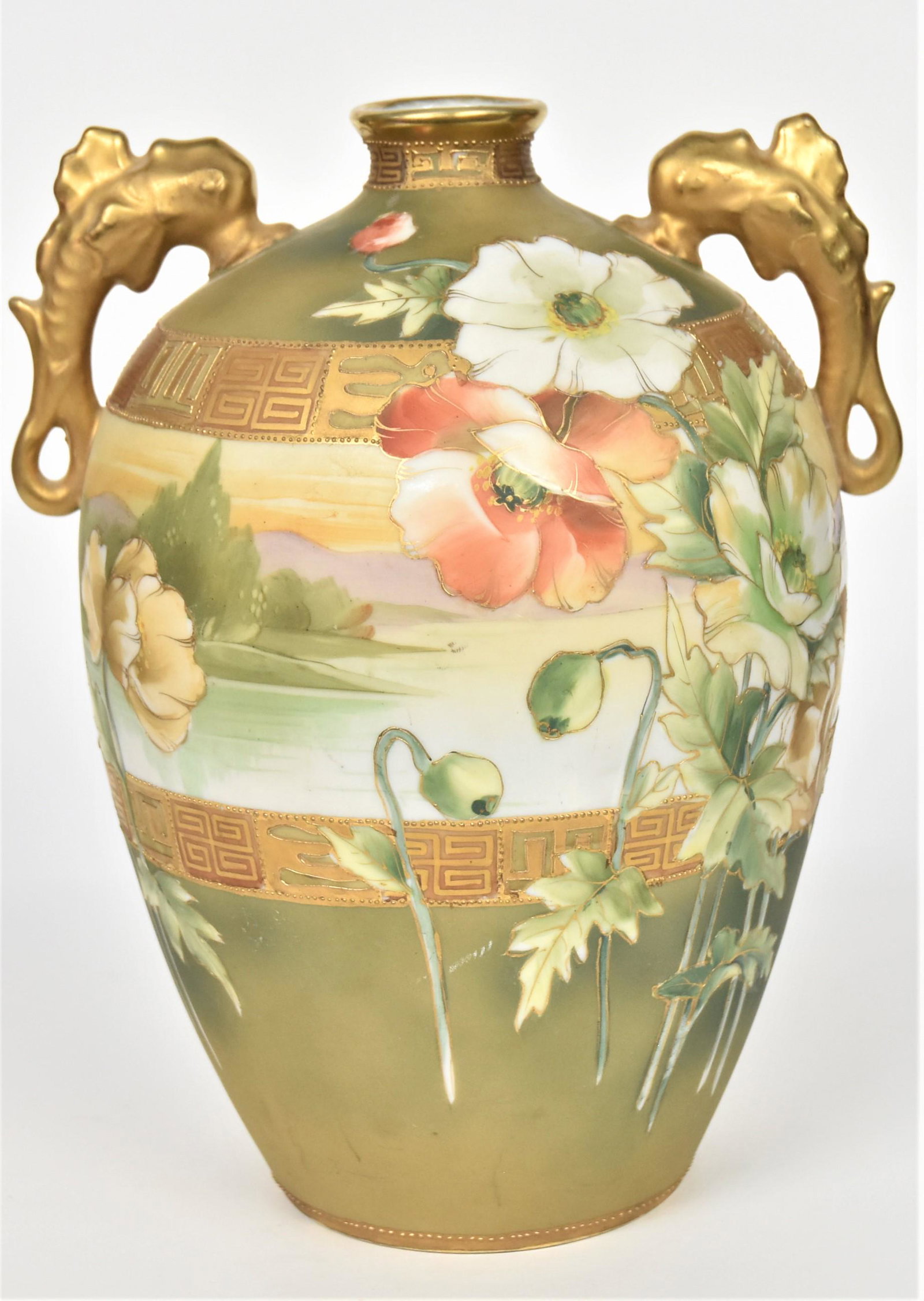 Nippon Dophin Handled Vase: Featuring stalks of white and coral poppies laid over a lake scene panel. Bordered by gold greek key design. 10 1/4"tall, 7 1/2" fin to fin. M in wreath backstamp. Impressive and in good condition.