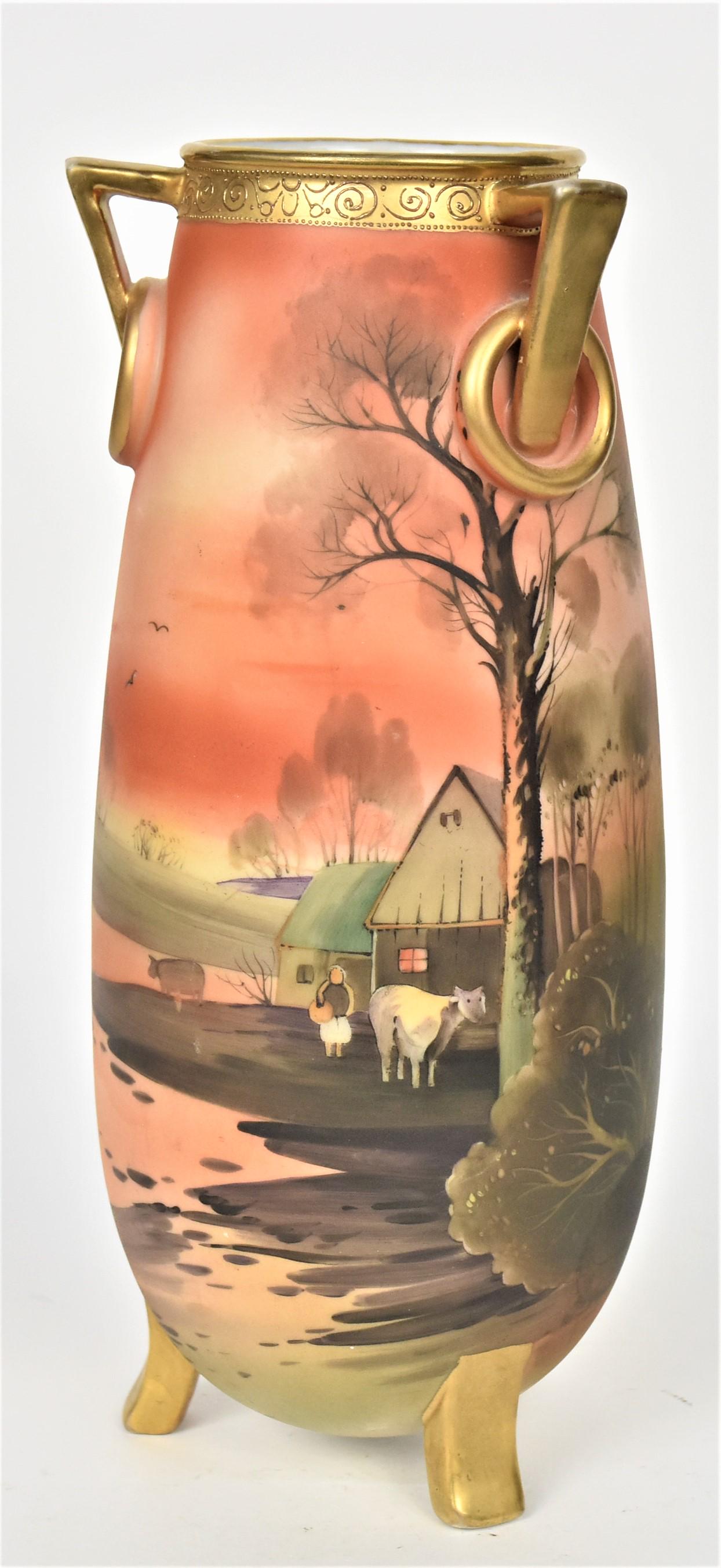 Nippon Scenic Vase with Ring Handles: With gold tri-handles and stationary rings, tri-footed feet. Lakeview farm setting of a barn, cows, and caretakers at eventide. 11 1/4" tall and 4 7/8" handle to handle, M in wreath backstamp.