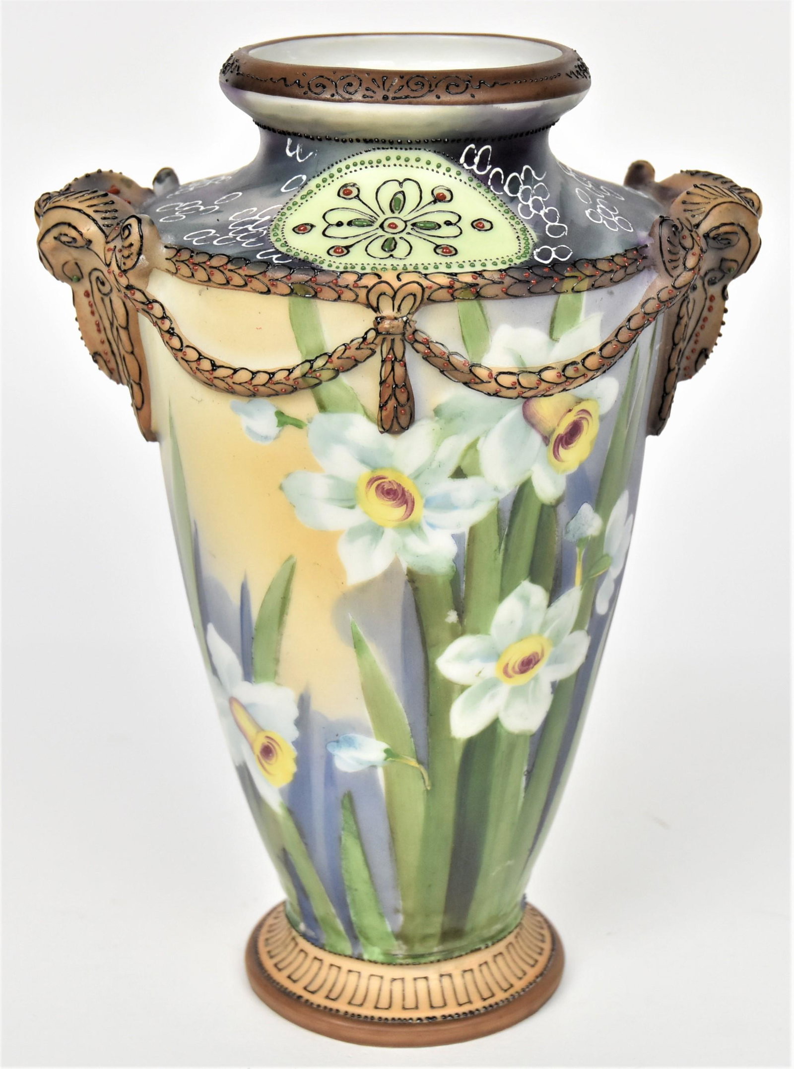 Nippon High Relief Rams Head Vase: With rams head shoulder ornaments with tasseled roping accented with enameling. Clumps of painted daffodils mainly on front. Jeweled flowers on shoulder. 9" tall, 6" rim to rim. Handsome vessel in goo