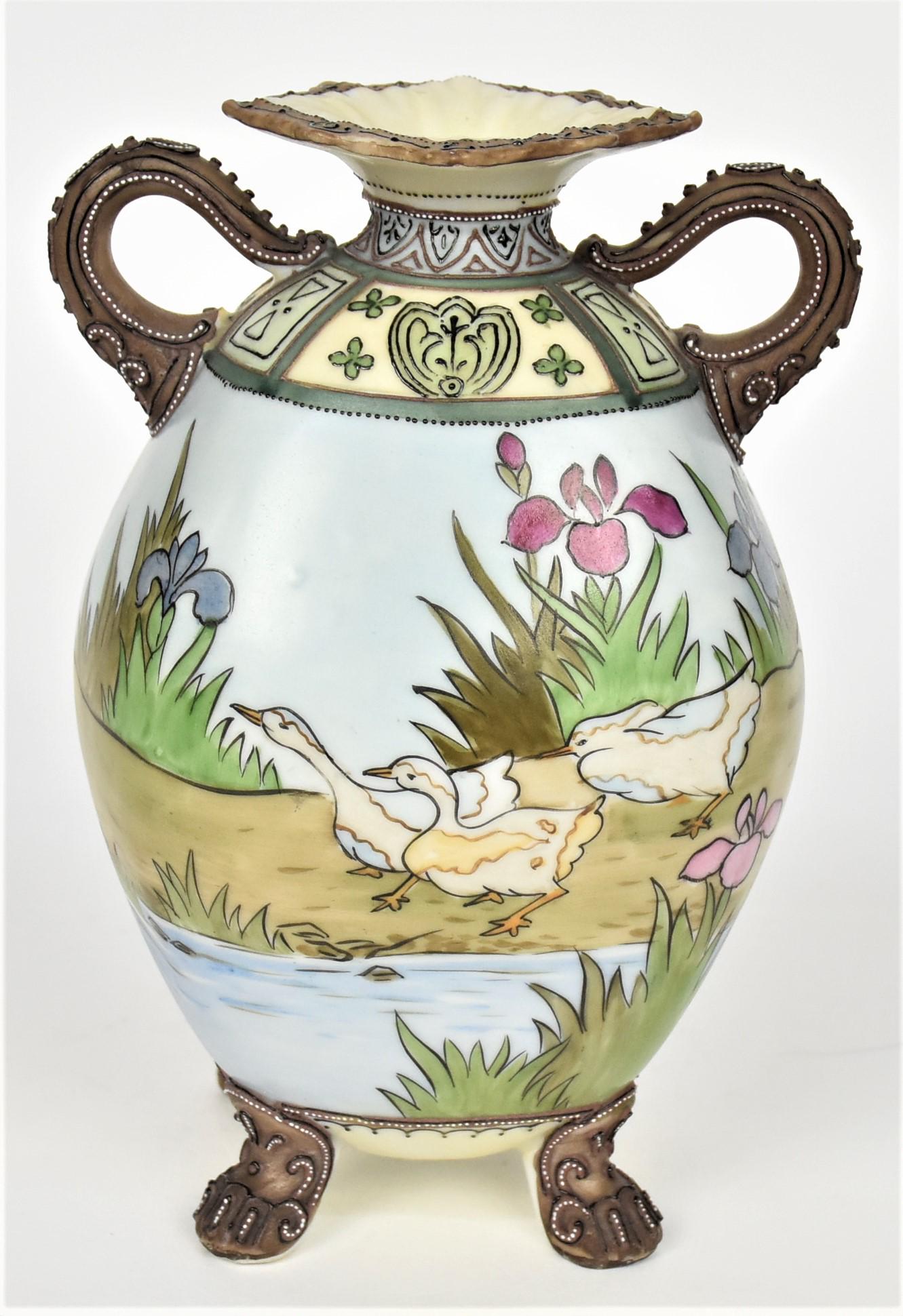 Nippon Moriage Duck Vase: With decorative squared rim, double handles and four feet. Painted with ducks and irises lakeside. Decorative enamel collar, 7 /4 tall, 5" handle to handle. M in wreath logo. Good condition.