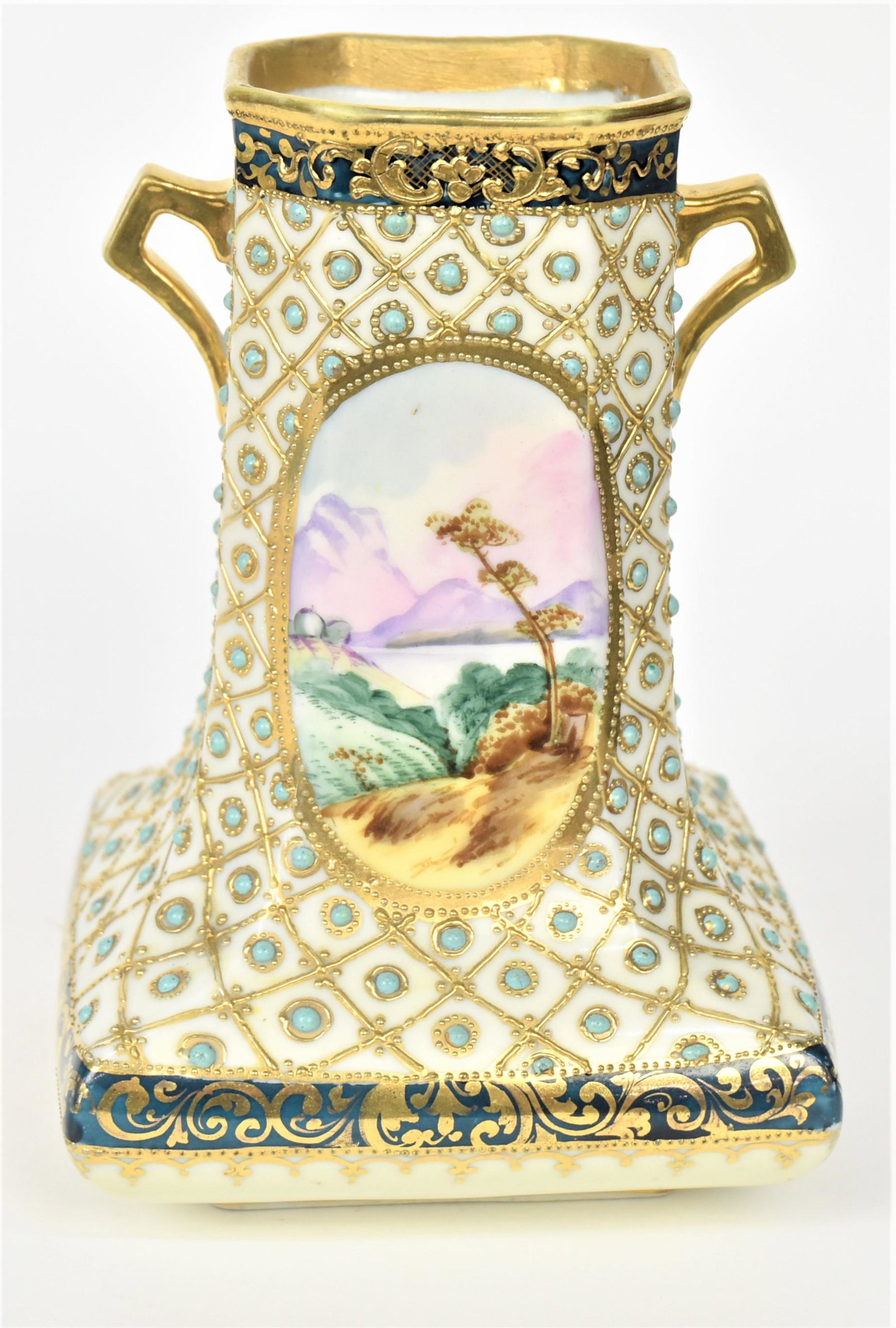 Nippon Netted and Jeweled Vase: Featuring turquoise enameled jewels and raised gold netting surrounding two scenic ovals, gold handles. 7" tall, 5" across base. Maple leaf logo. Corner bead missing, otherwise good Condition. Unusual