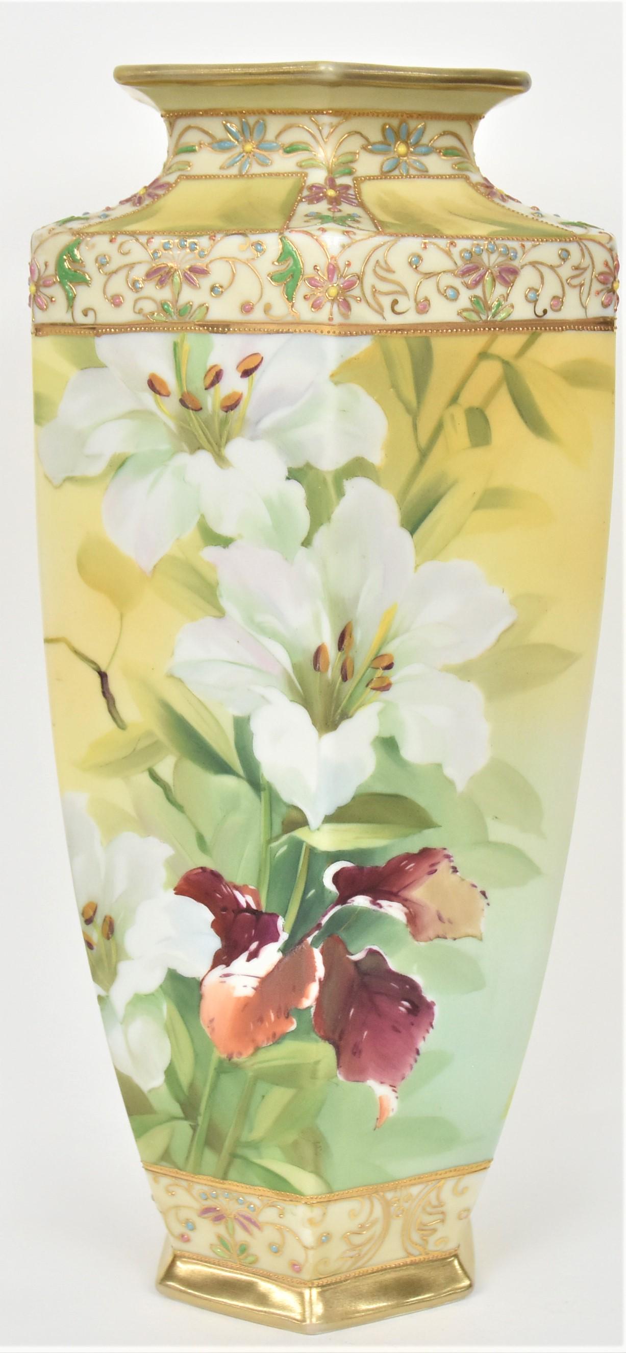 Tall Nippon Hexagonal Vase: Displaying white lilies on the front and a budding stalk on the reverse. Colorful enamel flowers and raised gold accents the shoulder and base. 13 1/2" tall, M in wreath logo. Highly attractive and in