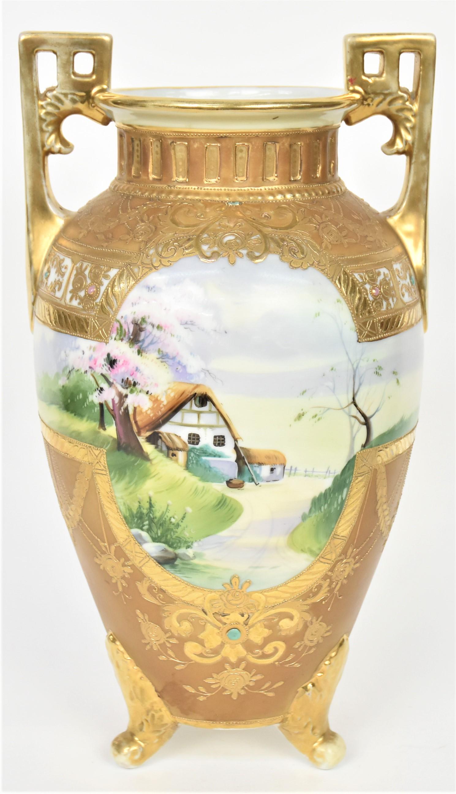 Large Nippon Jewel and Scenic Vase: Featuring a continous springtime landscape surrounded by elaborate raised gold floral and laural leaf motif. Reticulated gold collar, fancy pierced handles. Tri-footed acanthus leaf feet. 12 3/4"tall,
