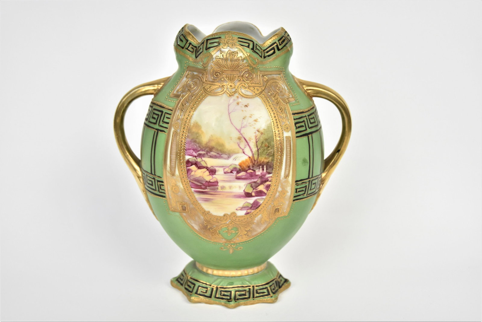 Nippon Blow-Out Scenic Vase: Scenic ovals front and back framed in raised gold greek key design. Good acanthus leaf handles, relief star-like base. 8 1/4" tall. A 2" line extends from rim, unnoticeable from exterior, otherwise go